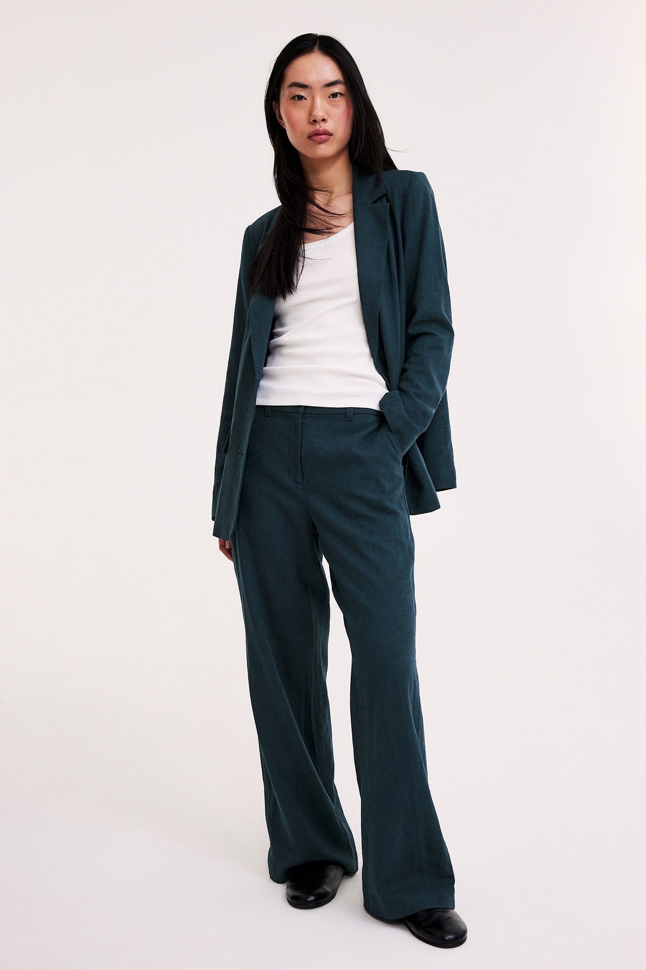 Frontvy av kvinne i mørkeblå melert lin dressbukse, åpen blazer, hvit topp og svarte sko.