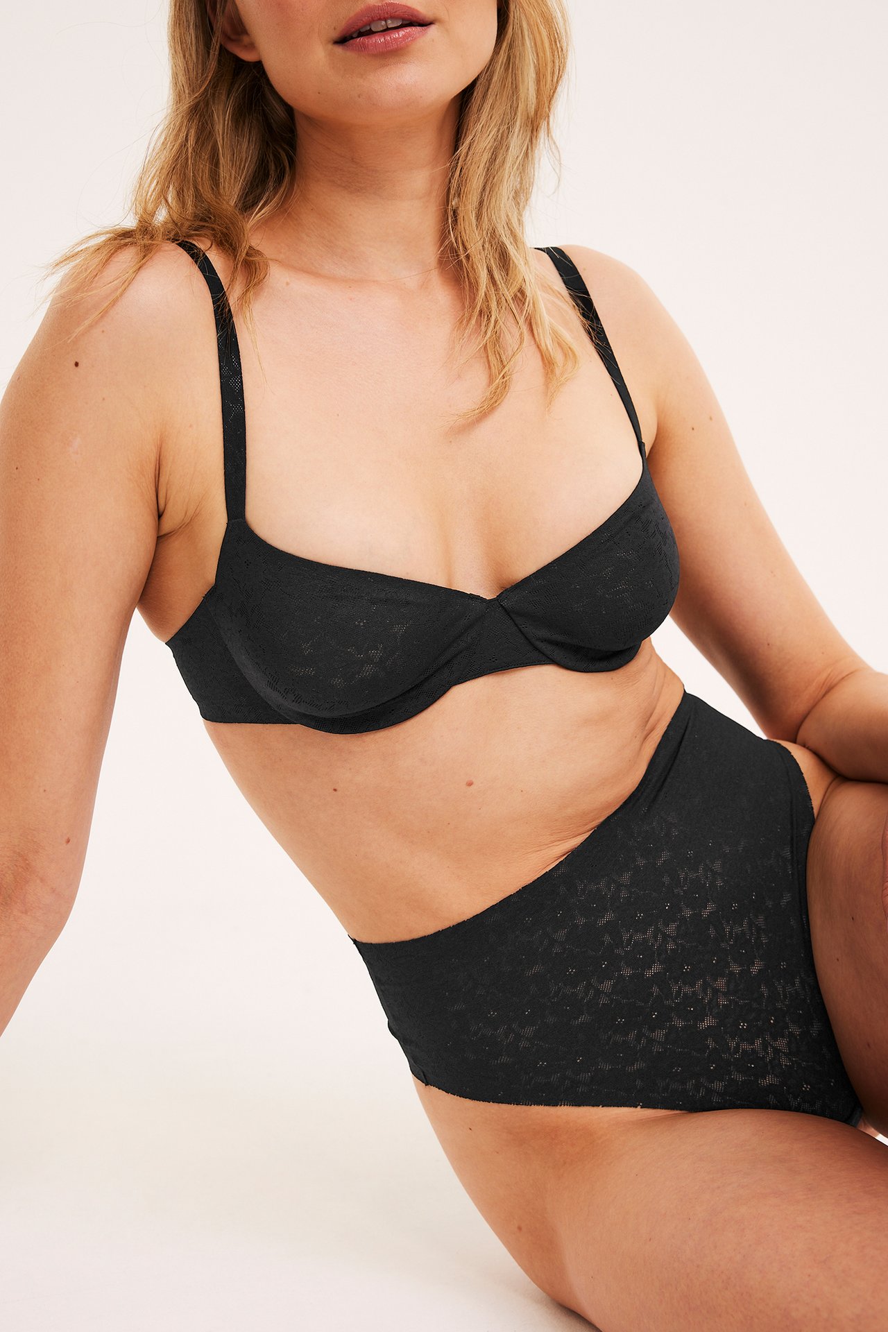 Frontvy av en kvinna som bär en svart bygel-bh i spets och matchande högmidjade spetstrosor.