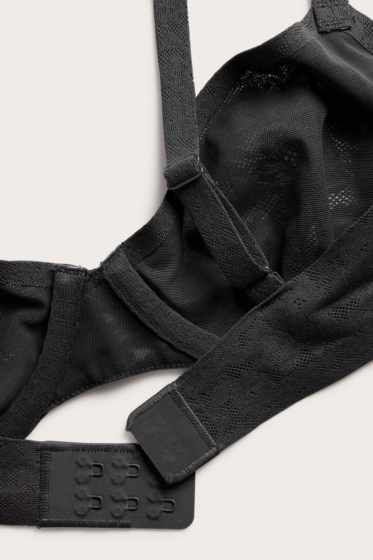 Zbliżenie czarnego, elastycznego biustonosza koronkowego na fiszbinach z regulowanymi ramiączkami i zapięciem na haftki.