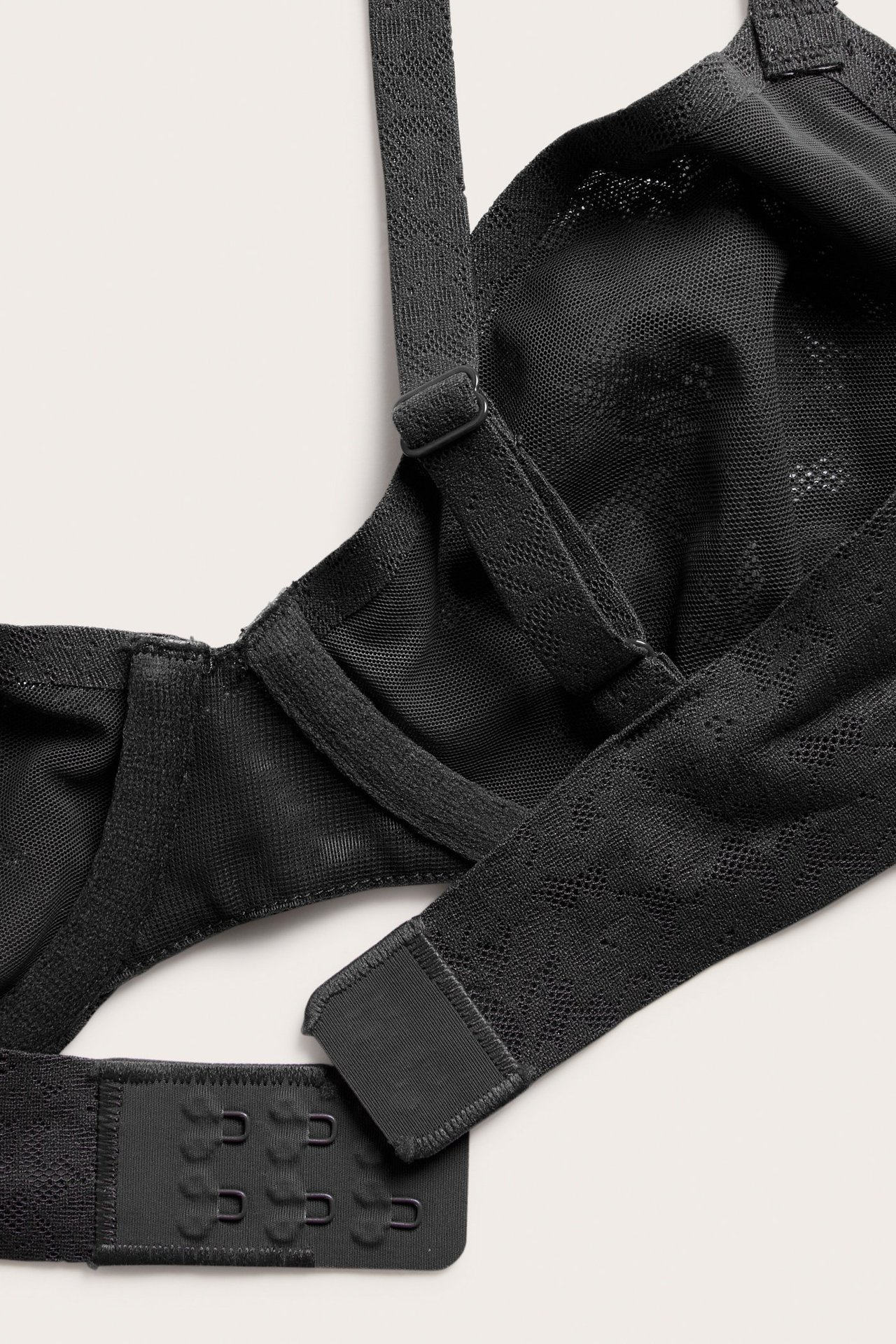 Zbliżenie czarnego, elastycznego biustonosza koronkowego na fiszbinach z regulowanymi ramiączkami i zapięciem na haftki.