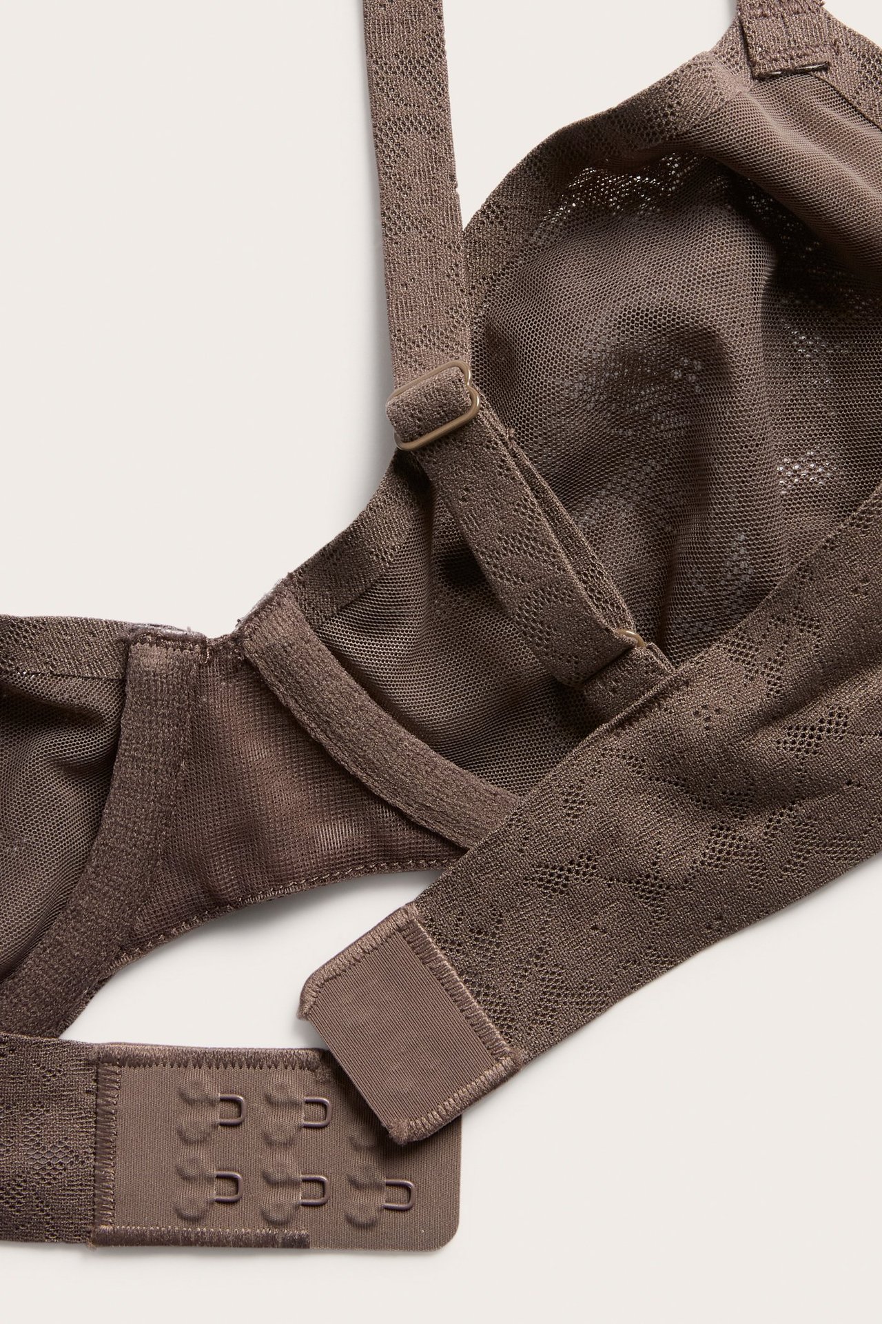 Zbliżenie na ciemnobrązowy biustonosz z fiszbinami z elastycznej koronki z regulowanymi ramiączkami i zapięciem na haftki.