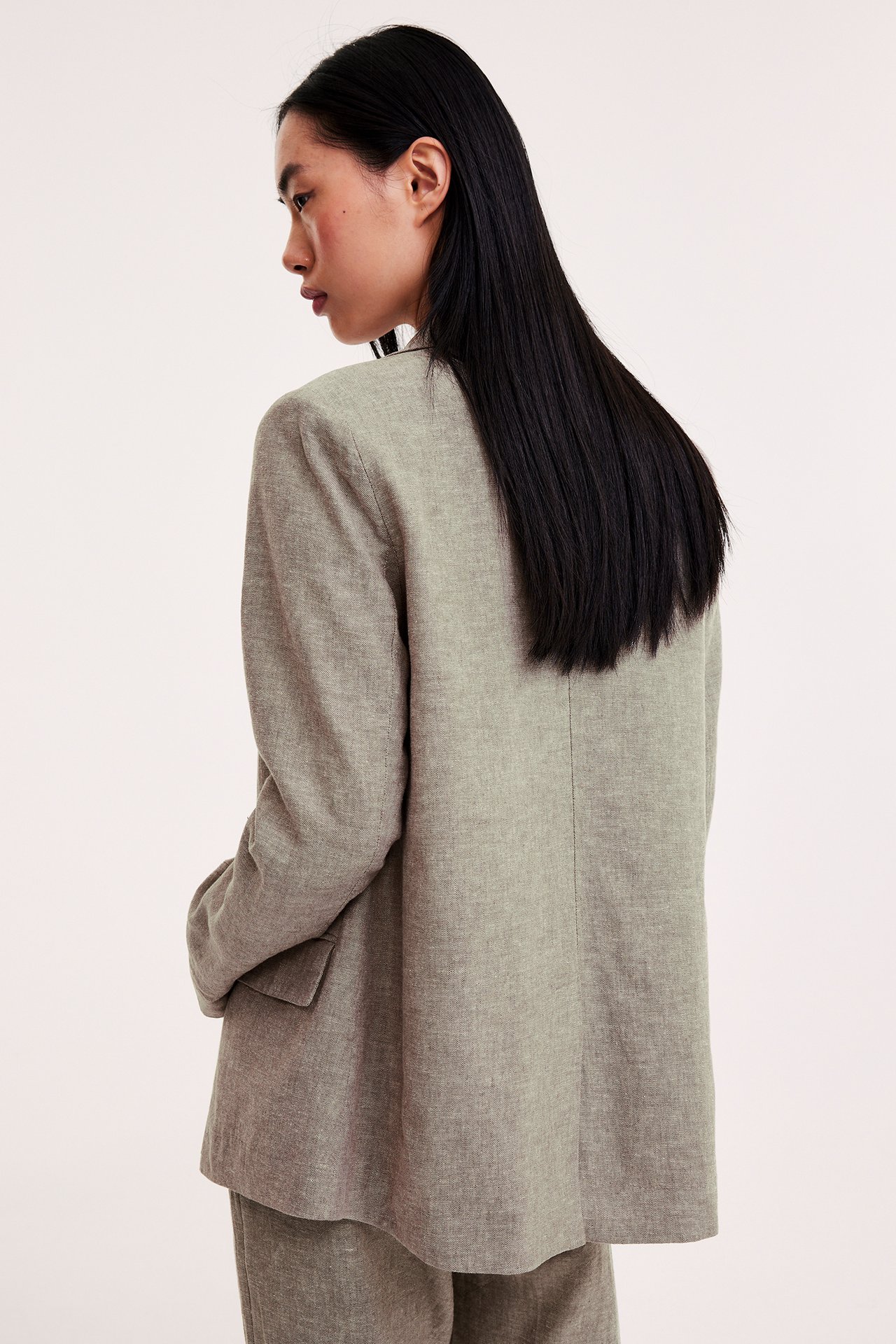 Sidovy bakifrån av en kvinna i en melerad brun linneblandningskavaj och matchande byxor.