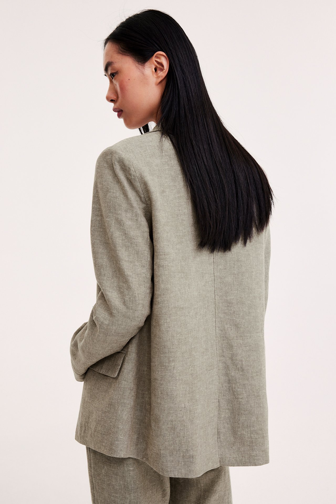 Nainen selkäpuolelta: väljä, meleerattu ruskea pellavasekoitekavaja ja yhteensopivat housut.