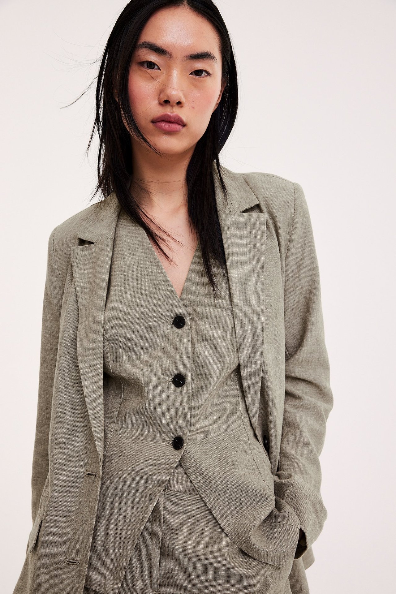 Frontvy av kvinna i brunmelerad linneblandad kavaj över matchande knäppt väst.