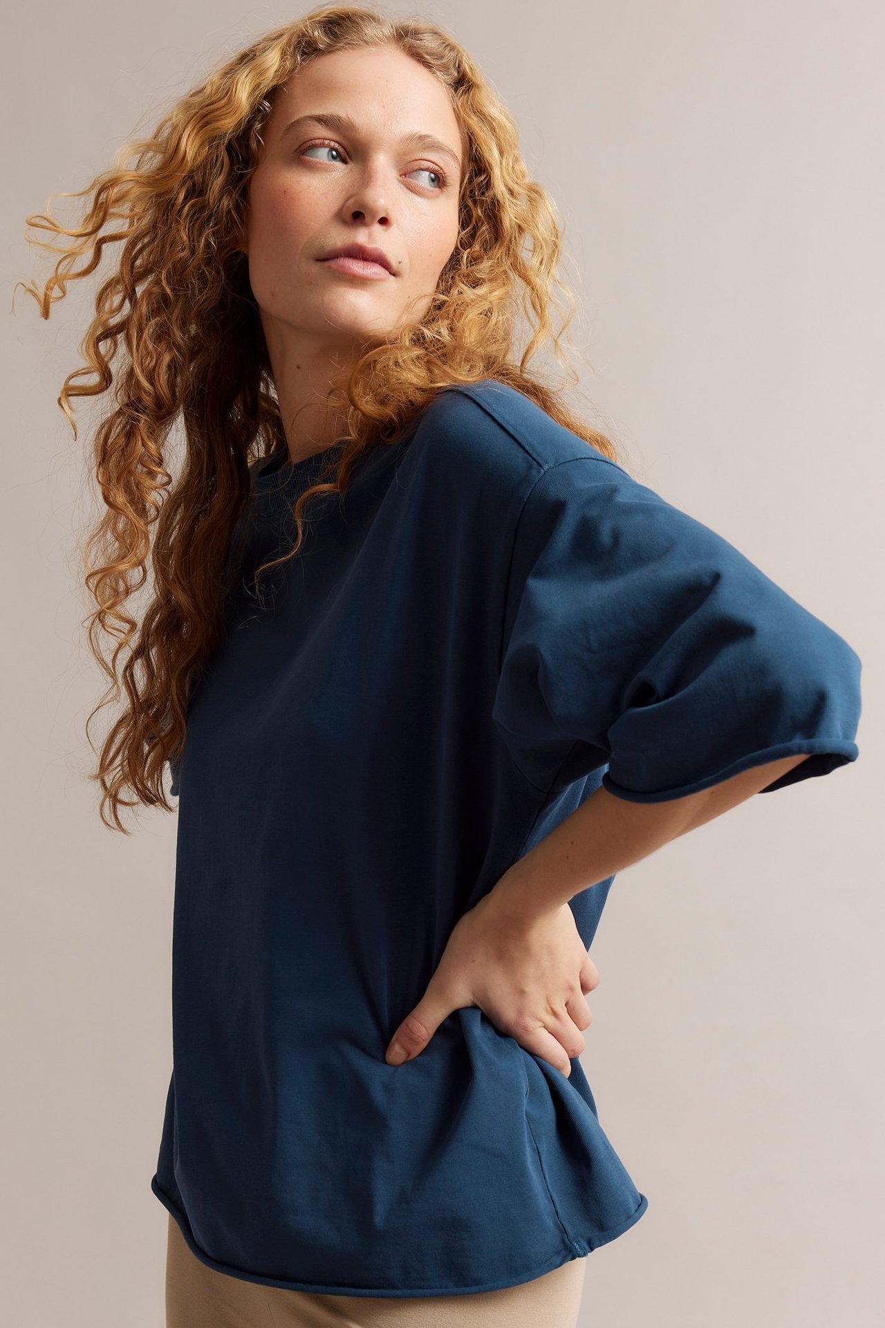Sivukuva naisesta löysässä sinisessä puuvilla-T-paidassa raakareunuksilla. Hänellä on vaaleanbeiget housut.