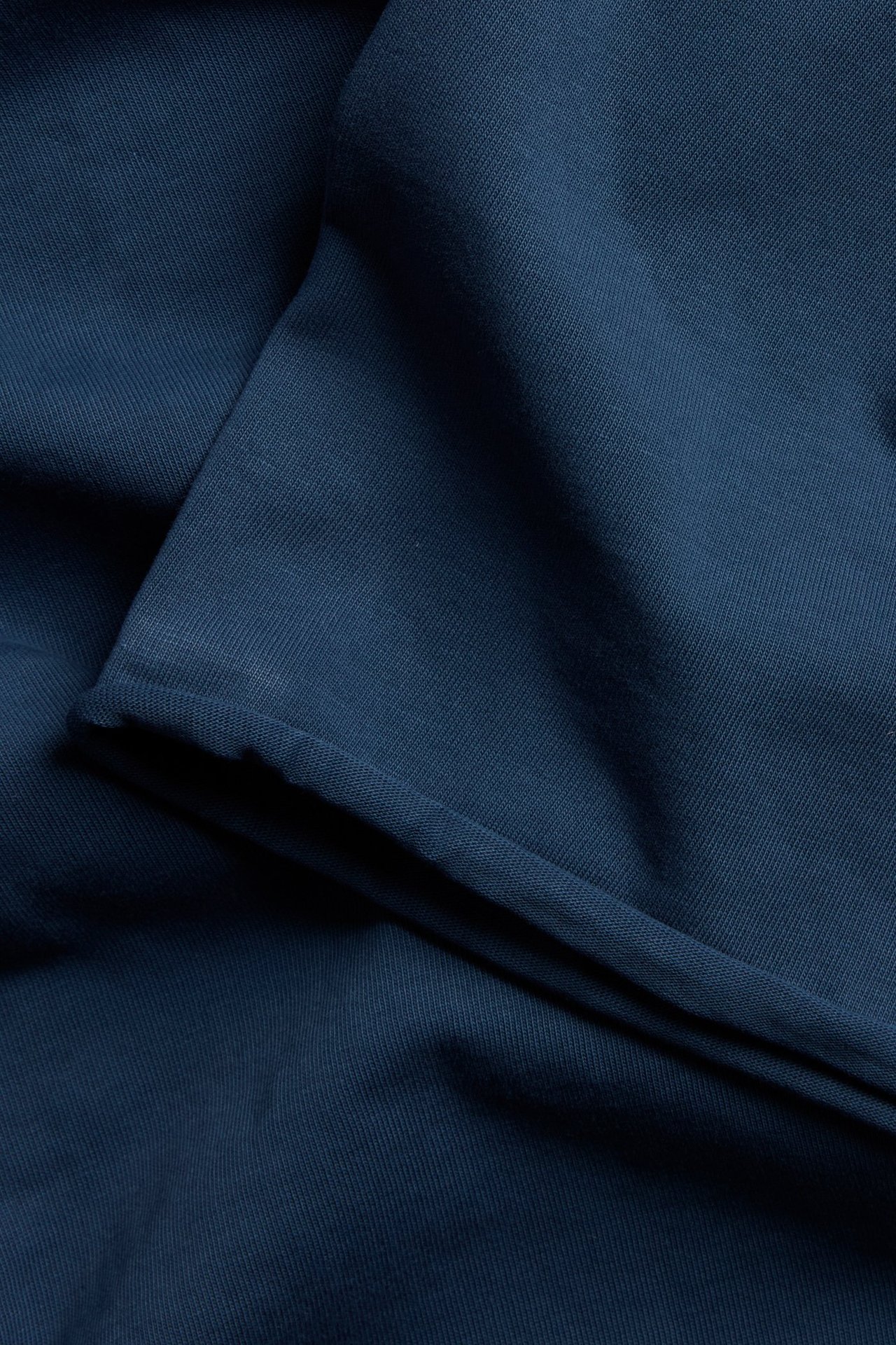 Zbliżenie niebieskiej bawełnianej koszulki z efektem sprania i surowymi obszyciami.