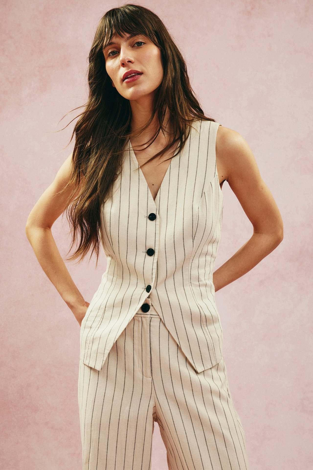 Widok z przodu kobiety w pasiastym, kremowym kamizelce lnianej z czarnymi guzikami i pasującymi spodniami.