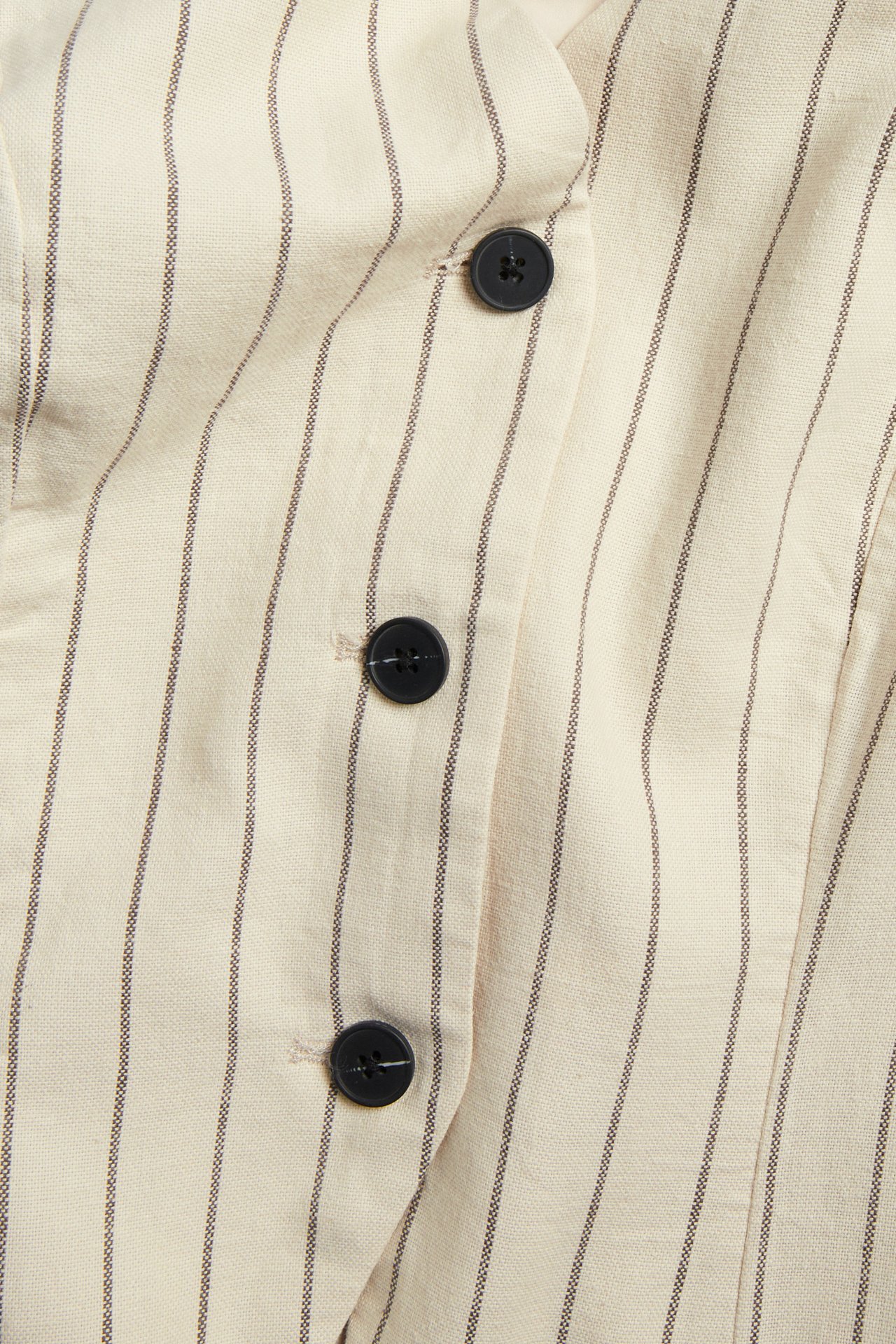 Lähikuva edestä luonnonvalkoisesta raidallisesta pellavaliivistä kapeilla raidoilla ja mustilla napeilla.