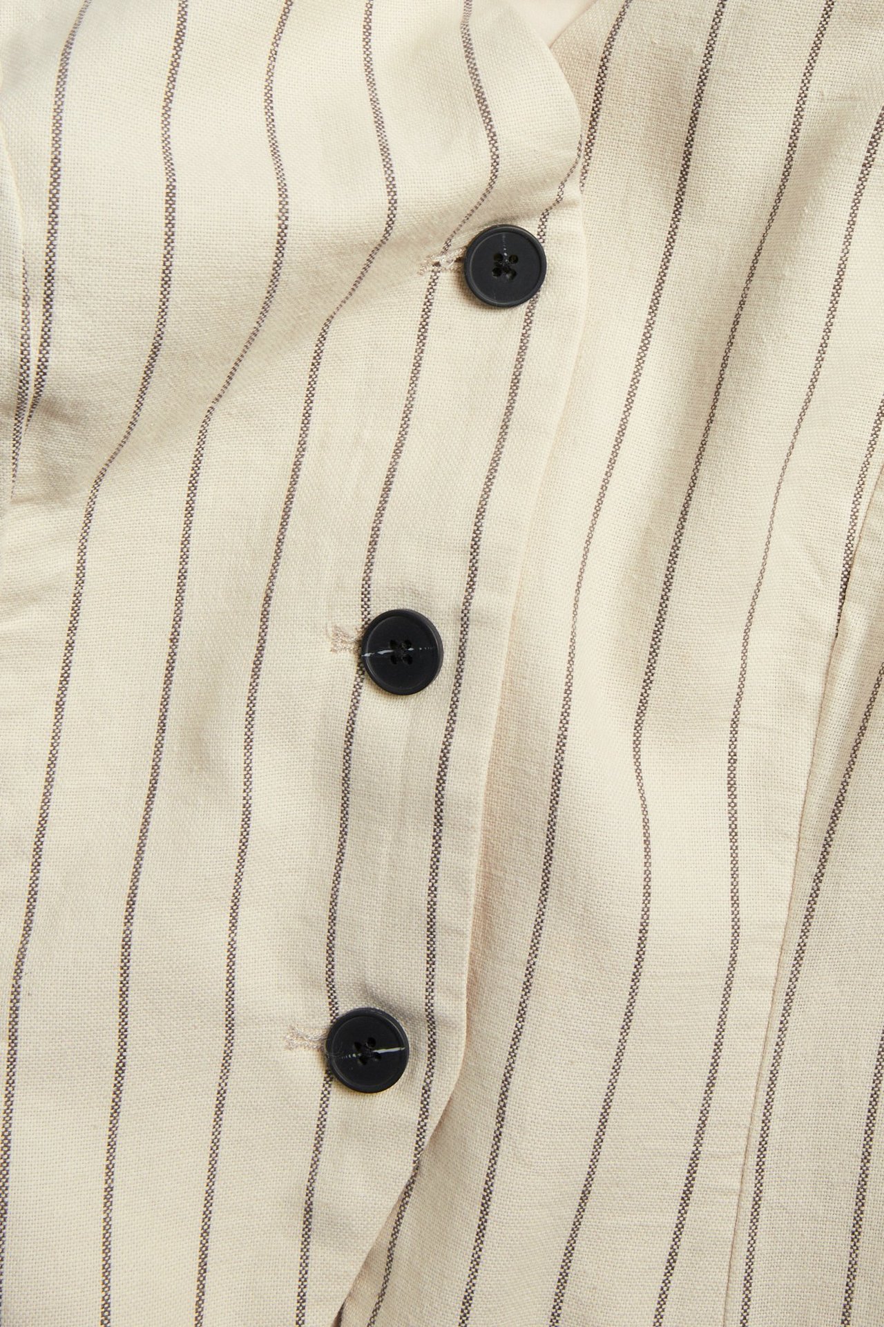 Zbliżenie przodu: biało-kremowa kamizelka z domieszką lnu, w cienkie paski, z czarnymi guzikami.