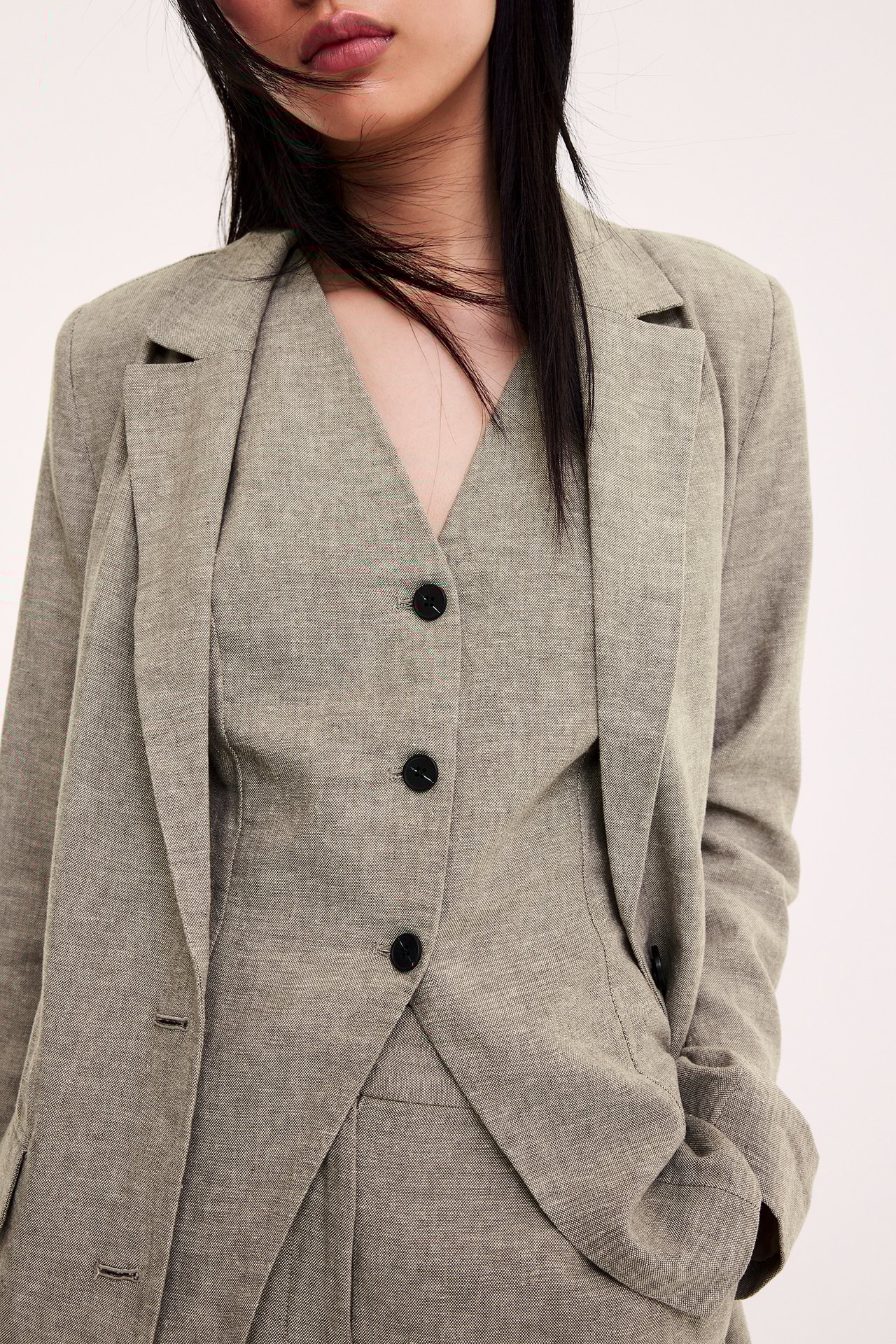 Lähikuva edestä: Nainen melange ruskeassa pellavasekoiteliivissä, mustilla napeilla ja bleiserissä.