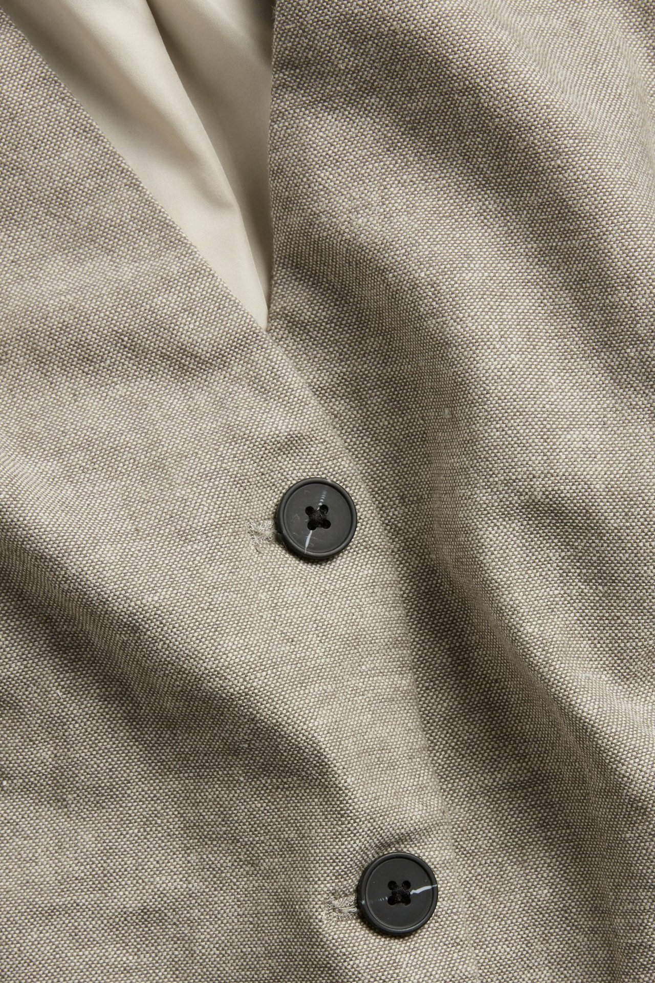 Nærbilde av en melert brun linblandingsvest med mørke knapper.