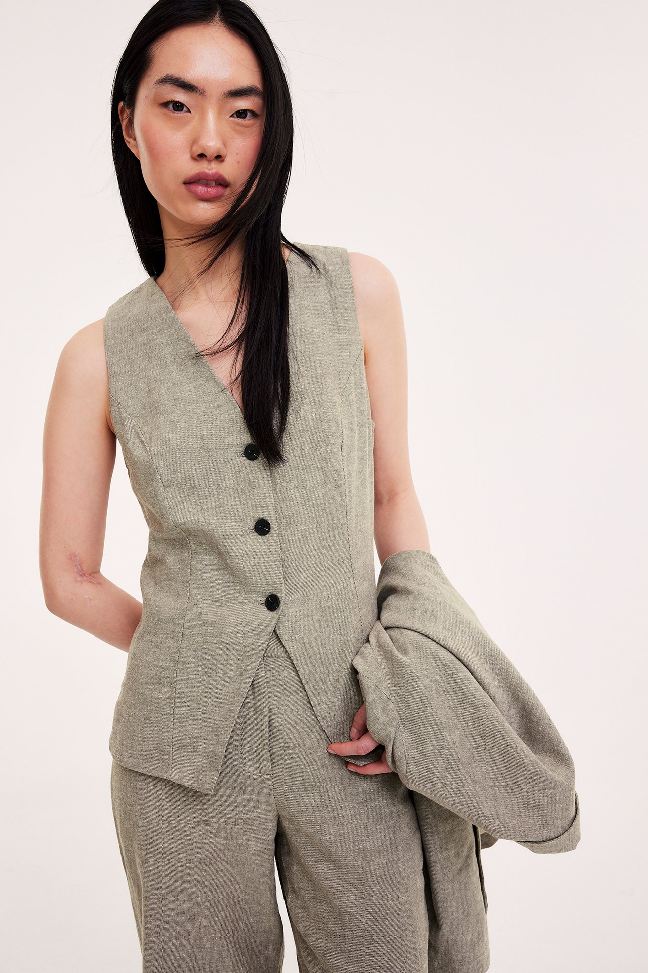 Edestä: Nainen kapeassa meleratussa ruskeassa liinavaateliivissä, yhteensopivissa housuissa ja bleiserissä.