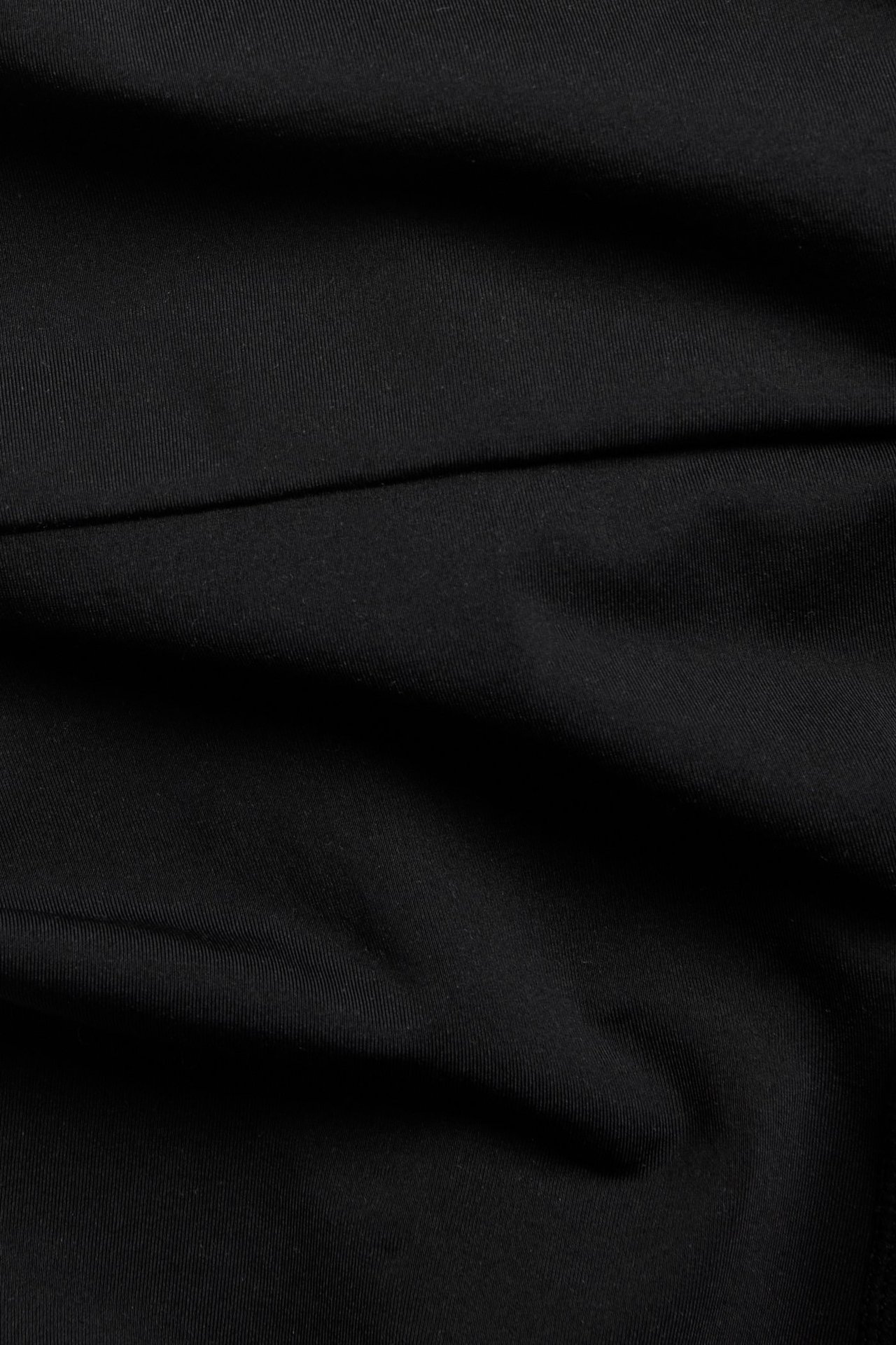 Närbild av svart enfärgat sömlöst shapingshorts-tyg med subtila veck.