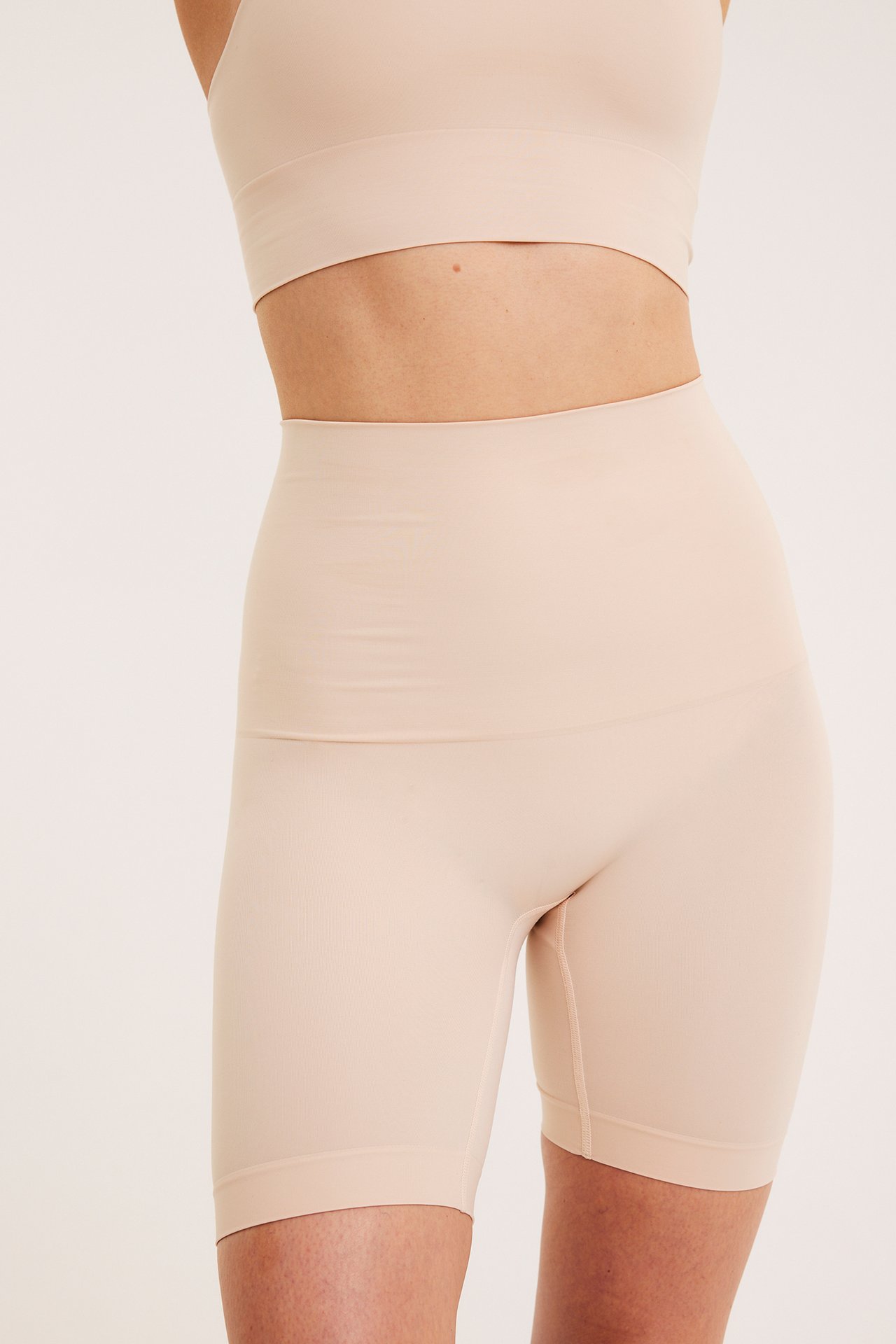 Widok z przodu: kobieta w jasnobeżowych bezszwowych szortach modelujących z wysokim stanem i topie.
