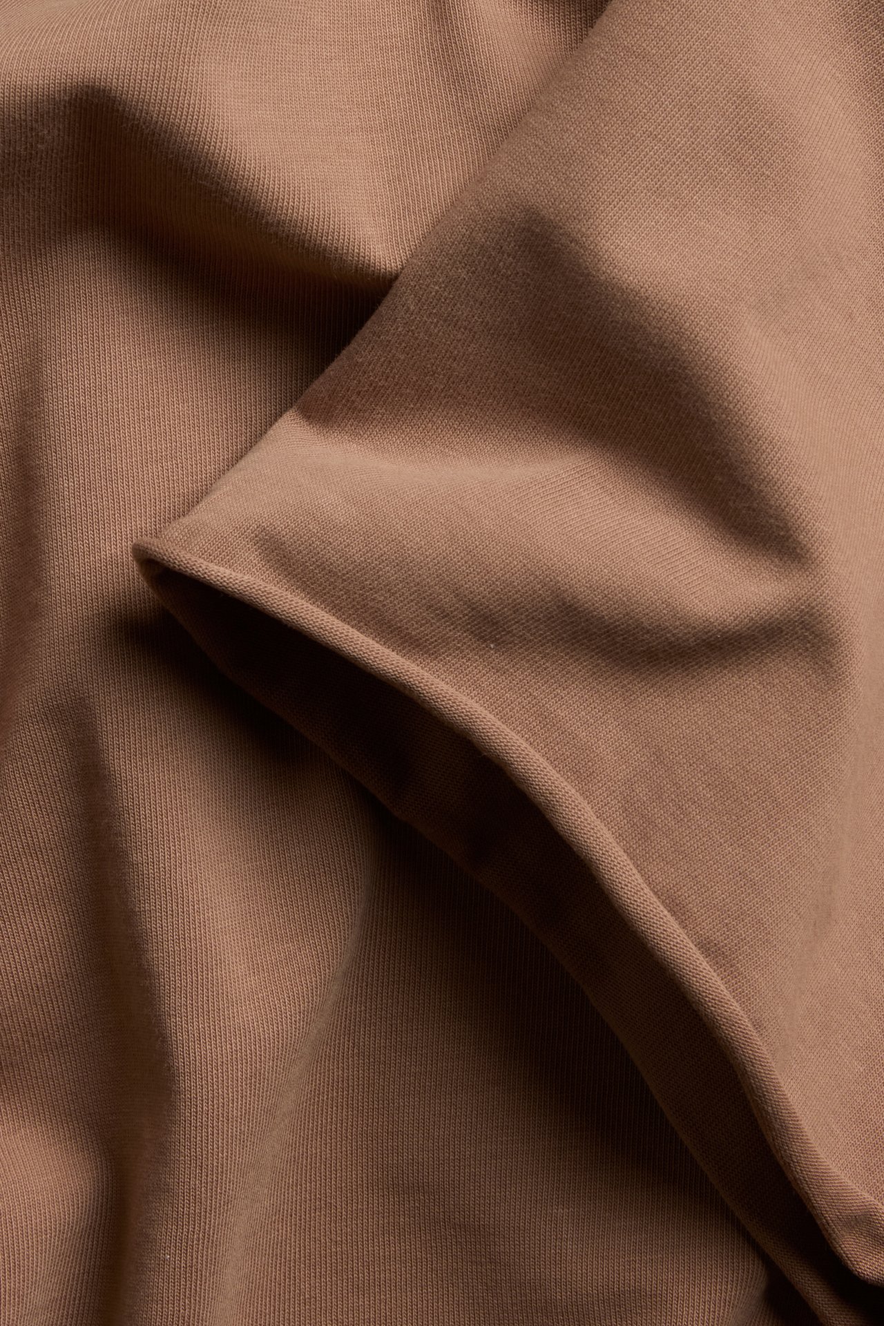 Nærbilde av brunt T-skjortestoff i bomull med tykk jerseystruktur og råkant.