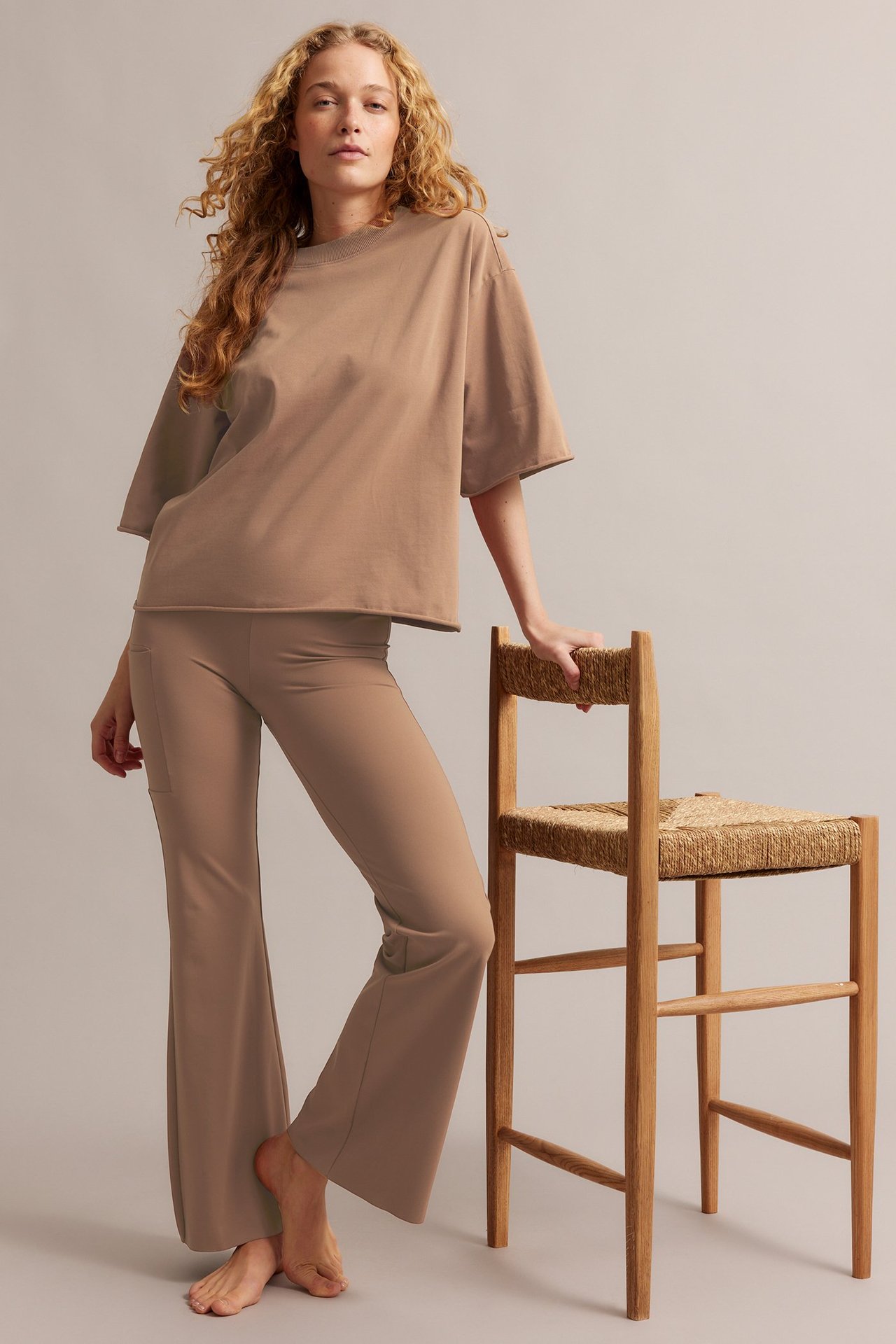 Widok z przodu: Kobieta w za dużej brązowej bawełnianej koszulce z surowymi brzegami i pasujących rozszerzanych spodniach.