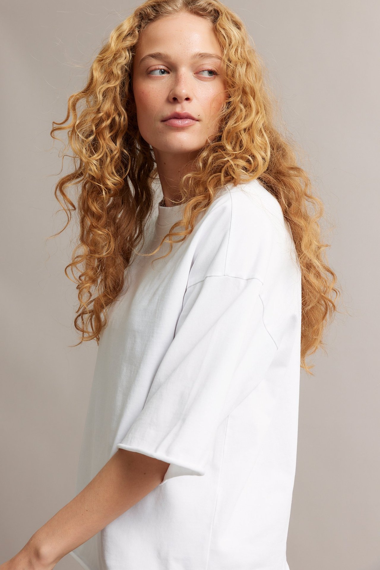 Sivukuva naisesta valkoisessa väljässä puuvilla-T-paidassa, jossa raakareunat ja pesukäsittely.