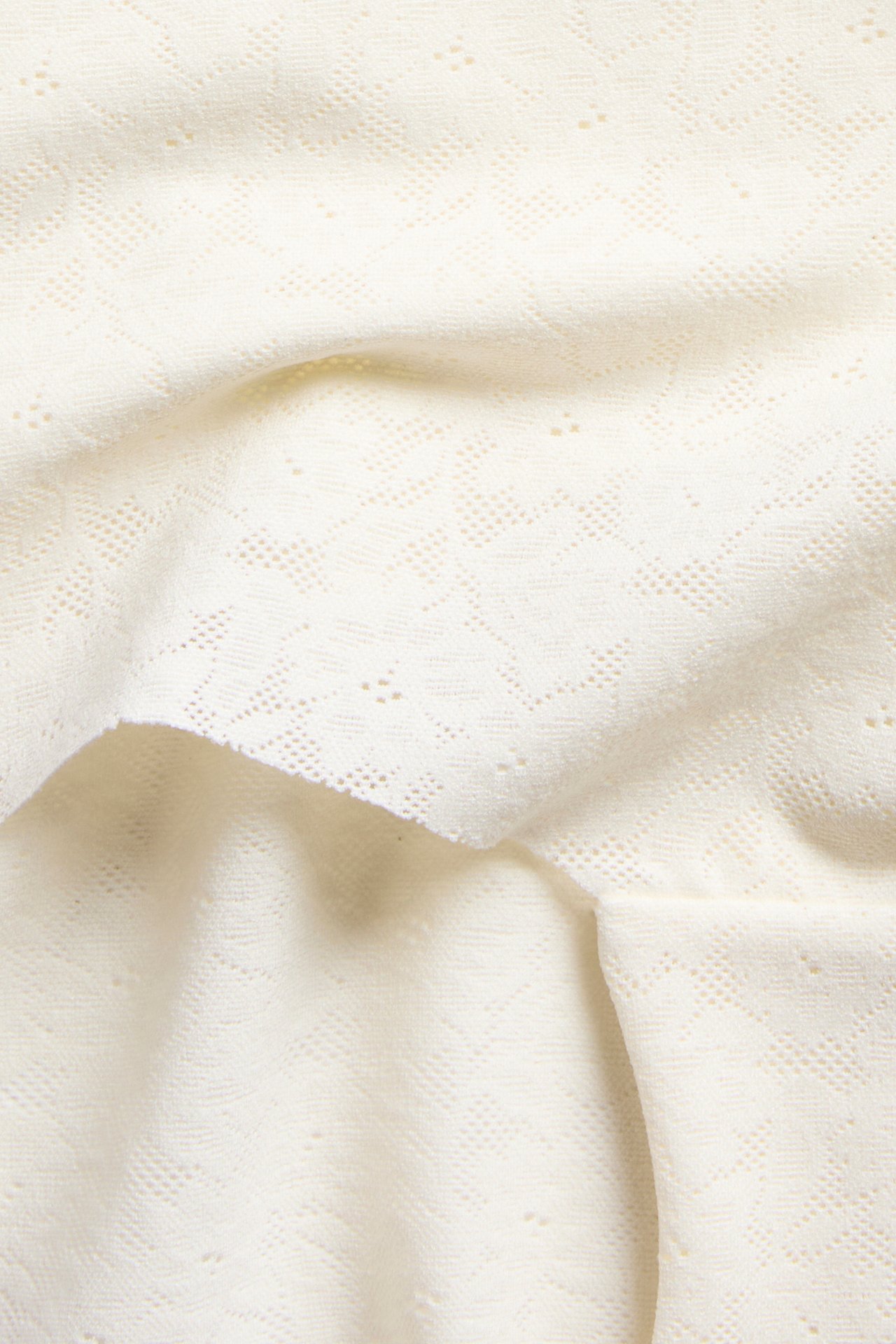 Närbild av offwhite stretchigt spetstyg med ett diskret geometriskt mönster.