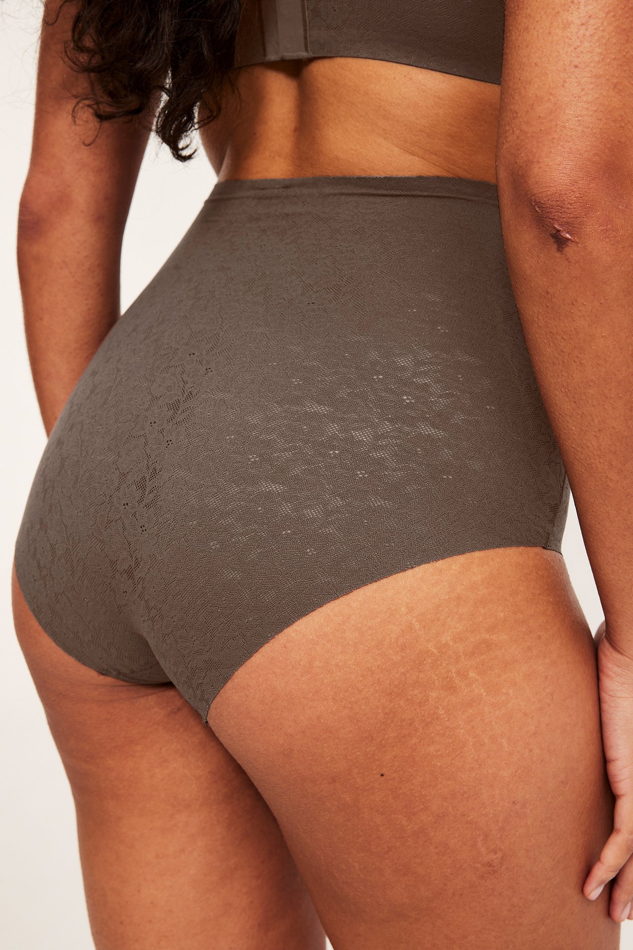 Bakfra, kvinne i mørkebrune høye blonde-hipster truser og matchende BH.