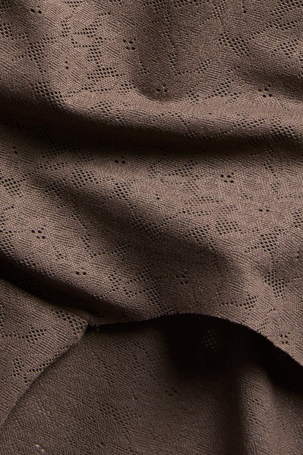 Närbild av mörkbrun, stretchig spetshipstertrosa med ett geometriskt mönster.