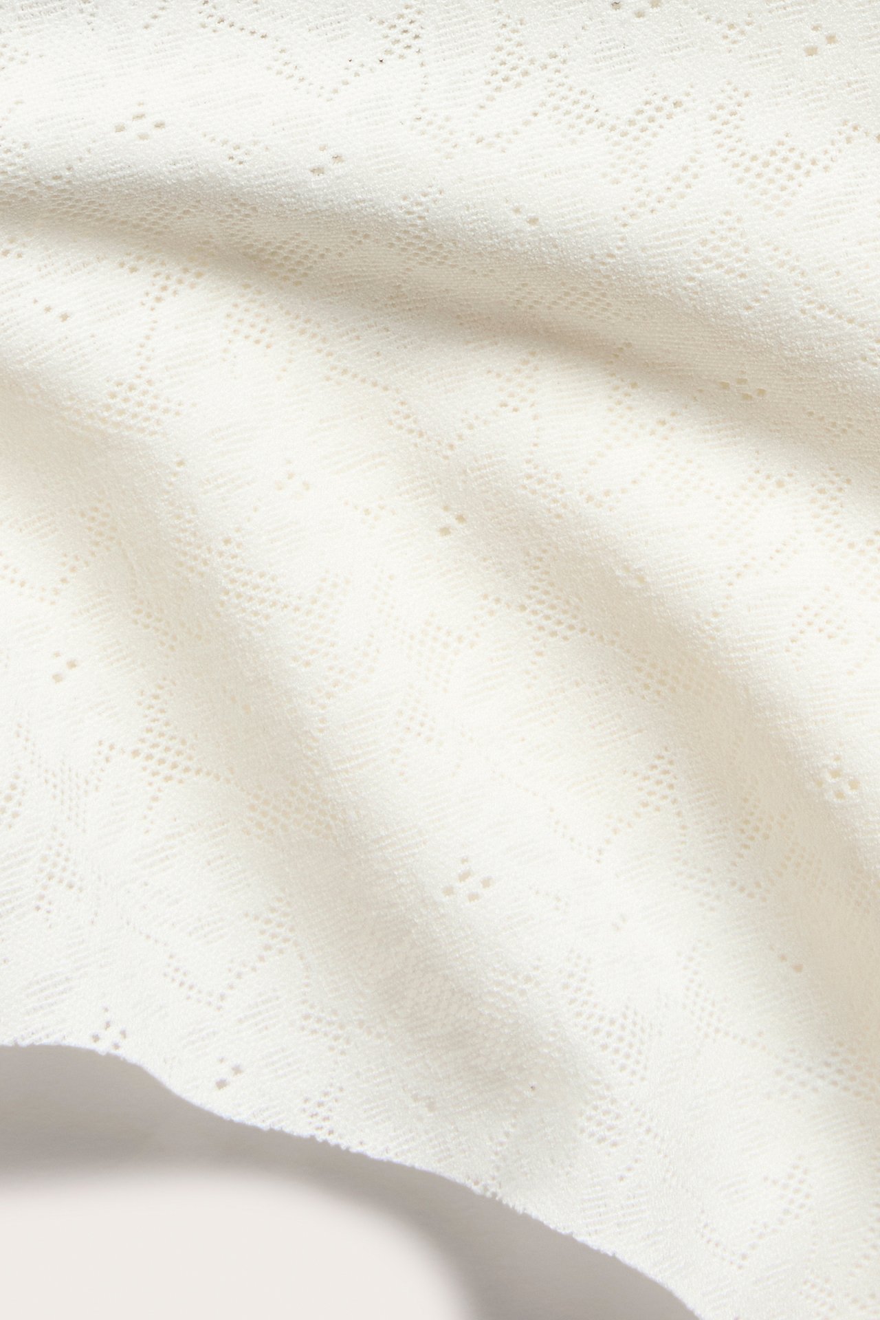 Zbliżenie na elastyczną koronkową tkaninę w kolorze ecru z subtelnym wzorem, idealną na niewidzialne stringi.