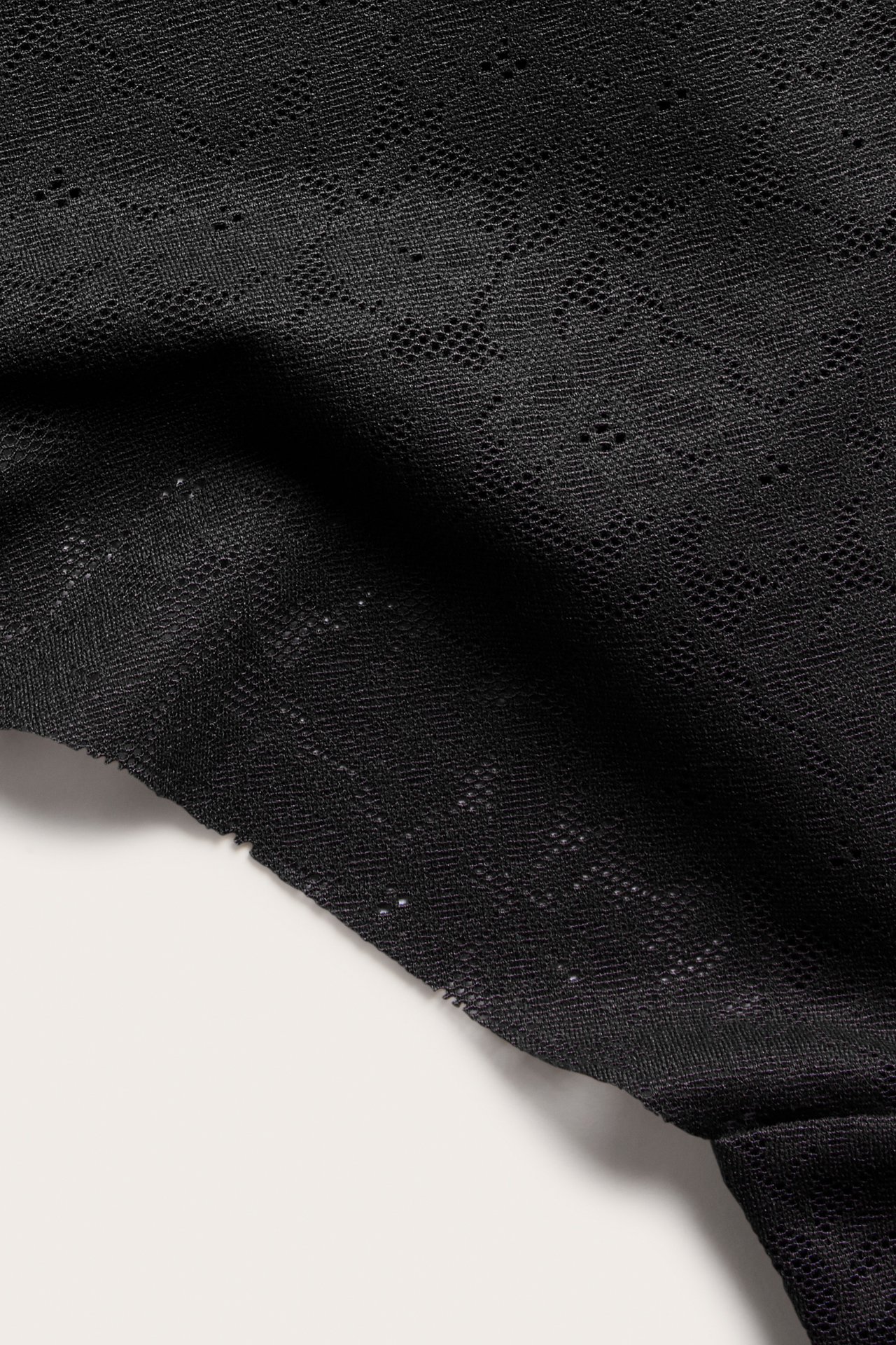 Zbliżenie na czarną koronkową tkaninę stringów, ukazującą rozciągliwy wzorzysty materiał.