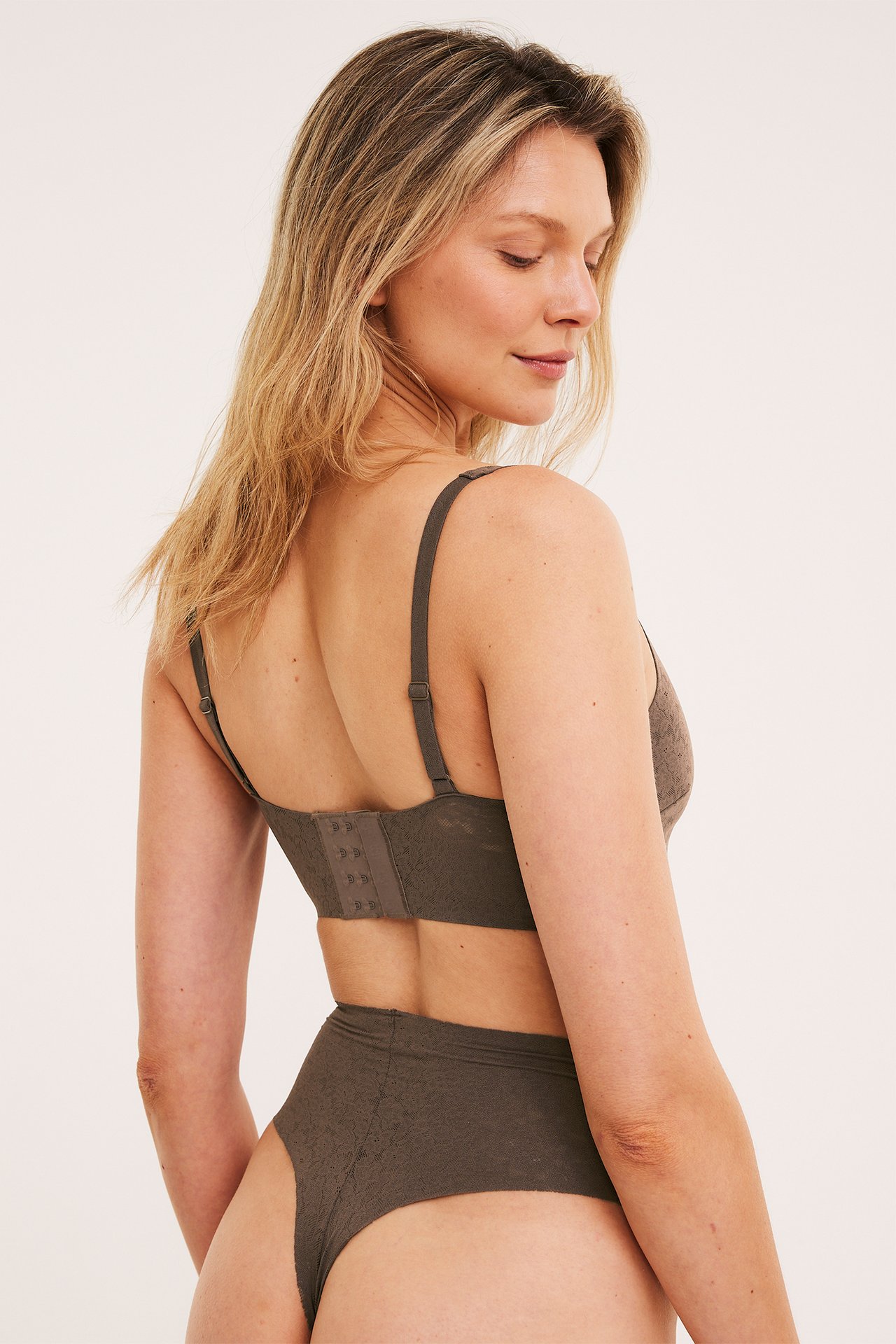 Bakifrån på kvinna i mörkbrun hög midja stretchspets stringtrosa och matchande spets-BH.