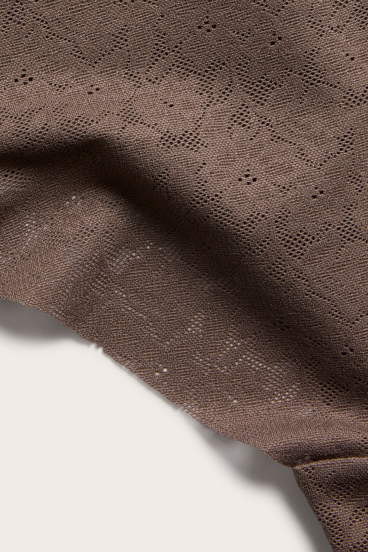 Zbliżenie na ciemnobrązowe, rozciągliwe koronkowe stringi z teksturowanym geometrycznym wzorem.