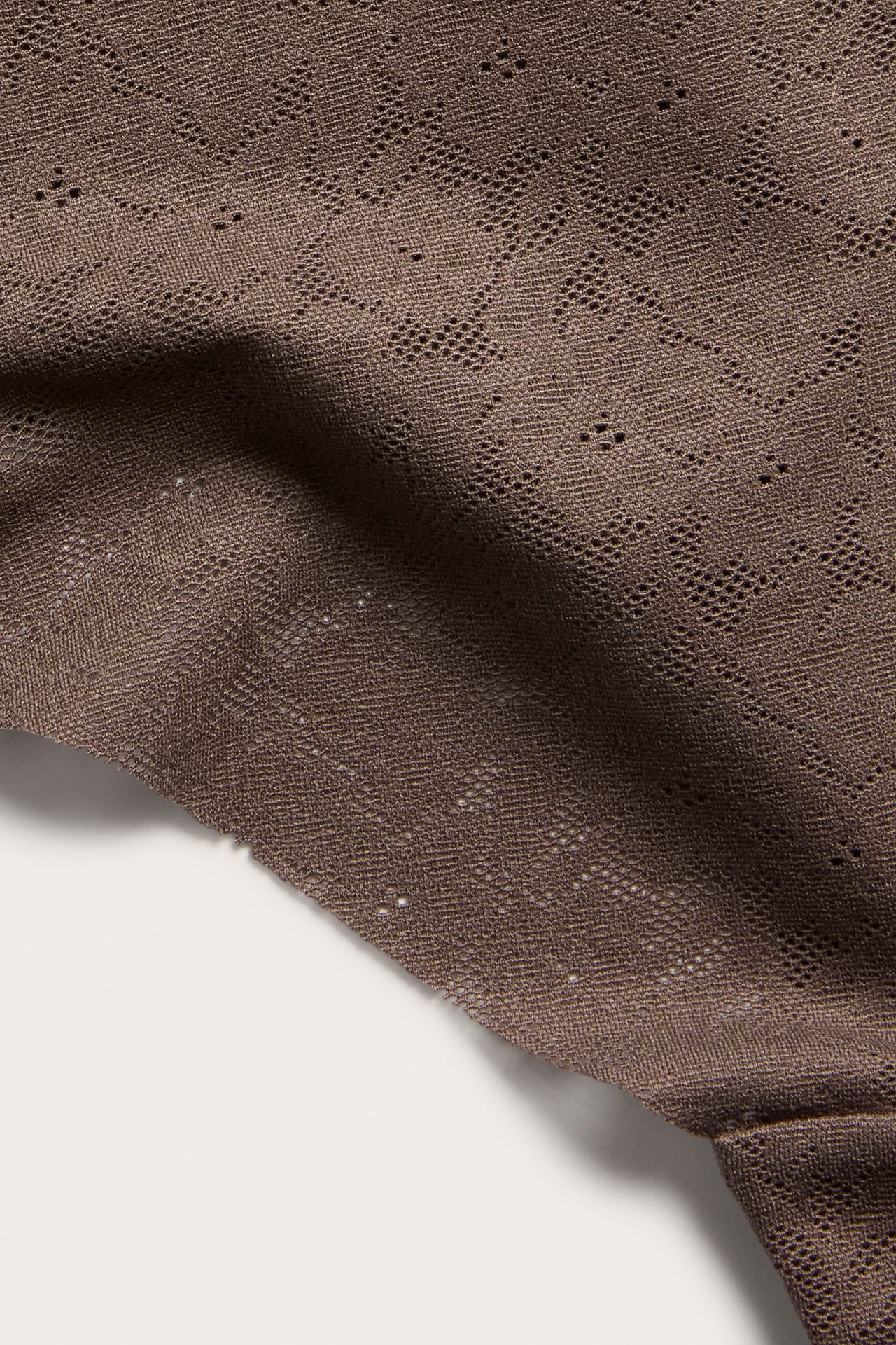 Zbliżenie na ciemnobrązowe, rozciągliwe koronkowe stringi z teksturowanym geometrycznym wzorem.