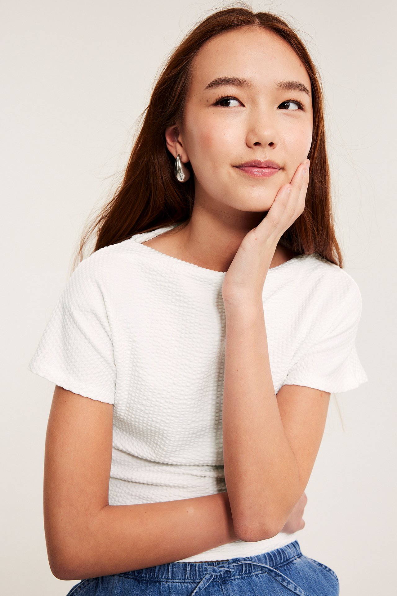 Framsida av flicka i vit kortärmad båtringad bäckebölja-topp och silverfärgade droppformade örhängen.