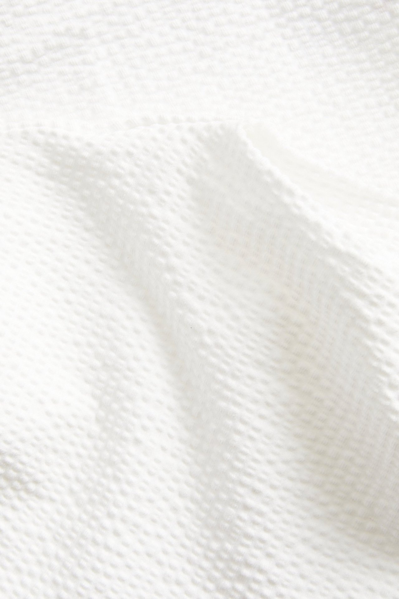 Lähikuva valkoisesta seersucker-paitatoppista, näyttää sen rypistyneen kangasrakenteen.