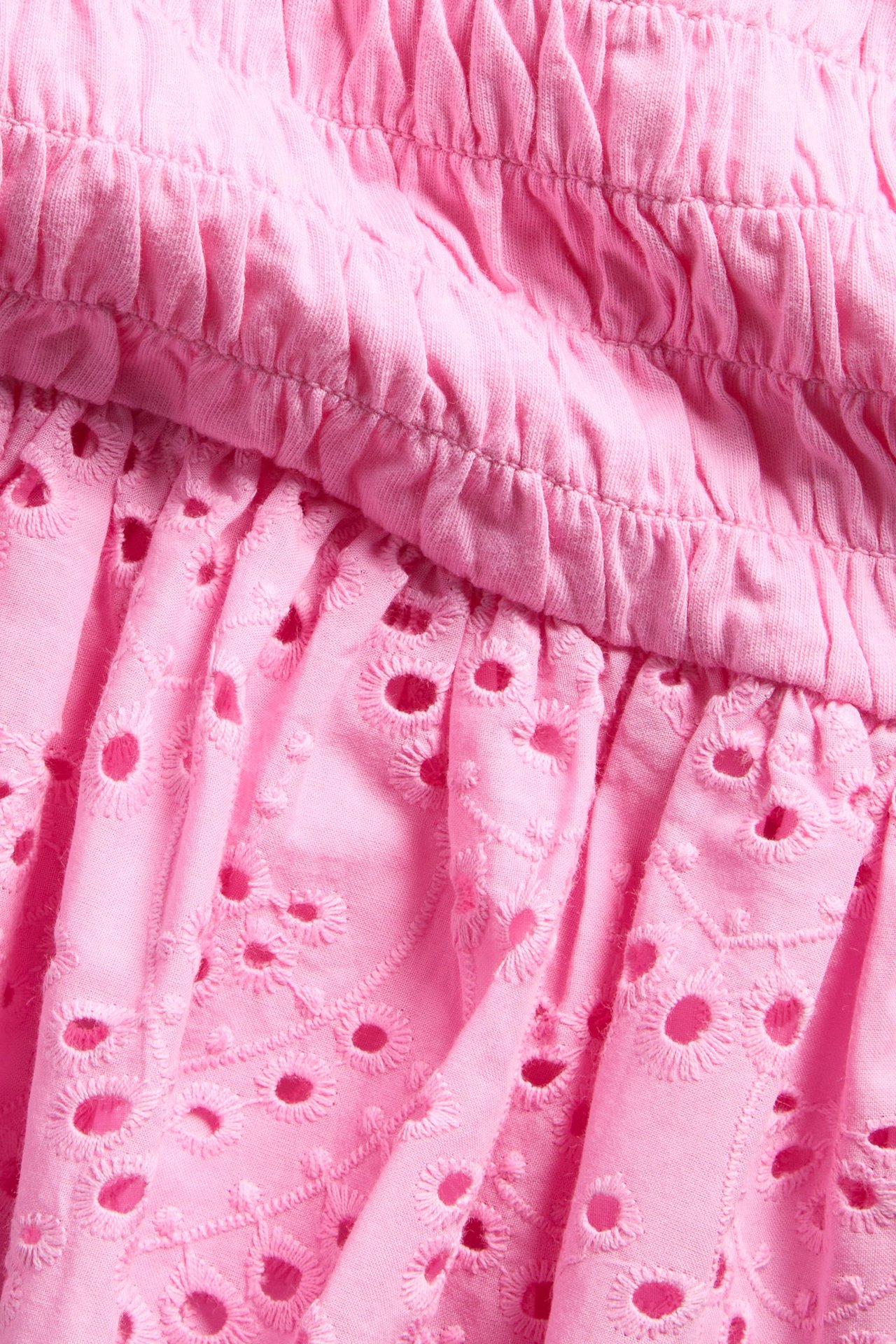 Zbliżenie różowego bawełnianego topu dziecięcego z marszczeniem, haftem angielskim i falbankami.