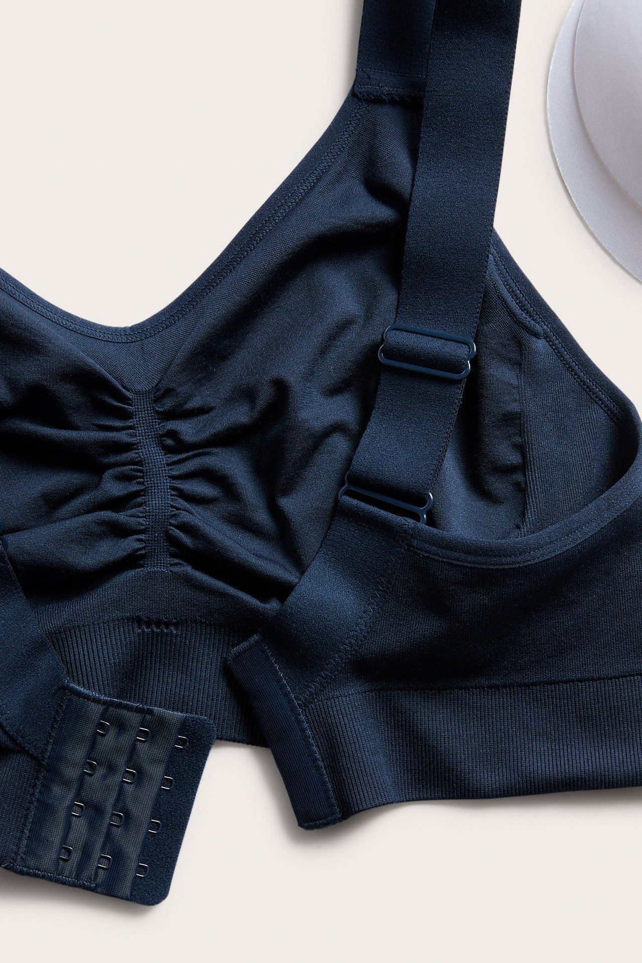 Nærbilde av mørkeblå sømløs bøyleløs BH med justerbare stropper, rynket front og hektefeste.