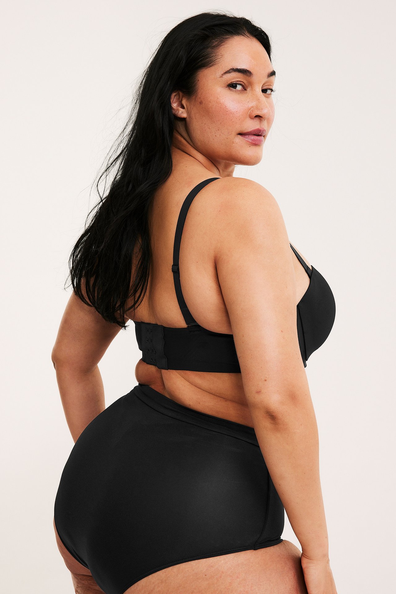 Kvinne i side-bakfra-visning, iført svart balconette-BH i mikrofiber med stropper og matchende truse.