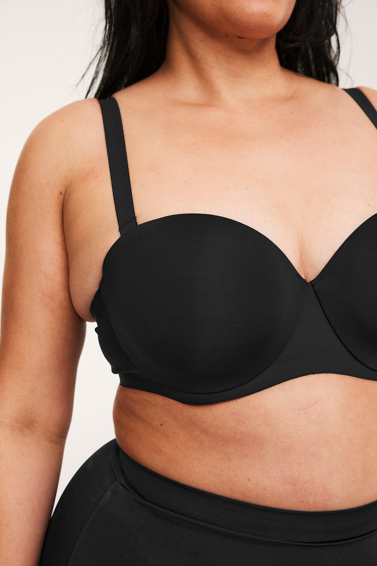 Lähikuva edestä naisesta mustissa mikrokankaisissa balconette-rintaliiveissä olkaimilla ja yhteensopivilla alaosilla.