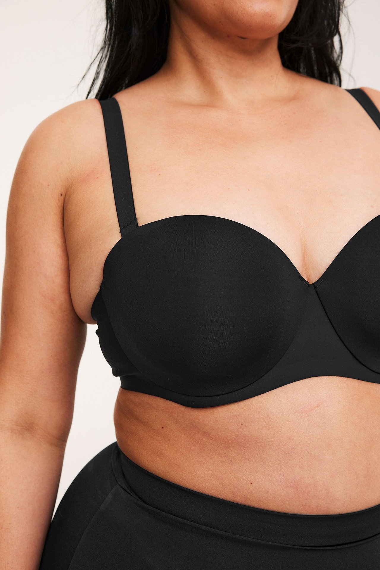Närbild framifrån av en kvinna i svart micro balconette-bh med axelband och matchande svarta trosor.