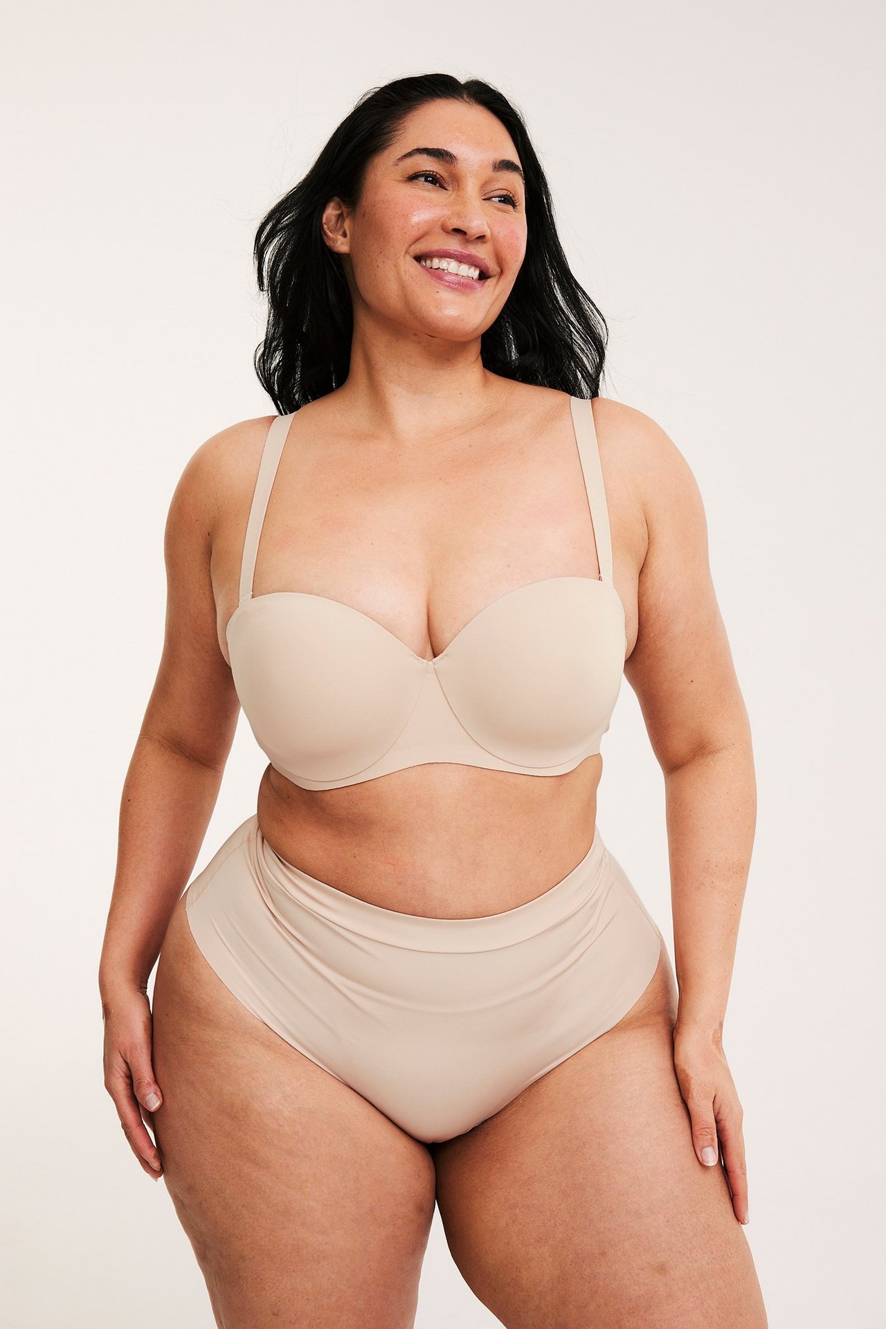 Frontvy: Leende kvinna bär en beige balconette-bh i micro med band och matchande trosor.