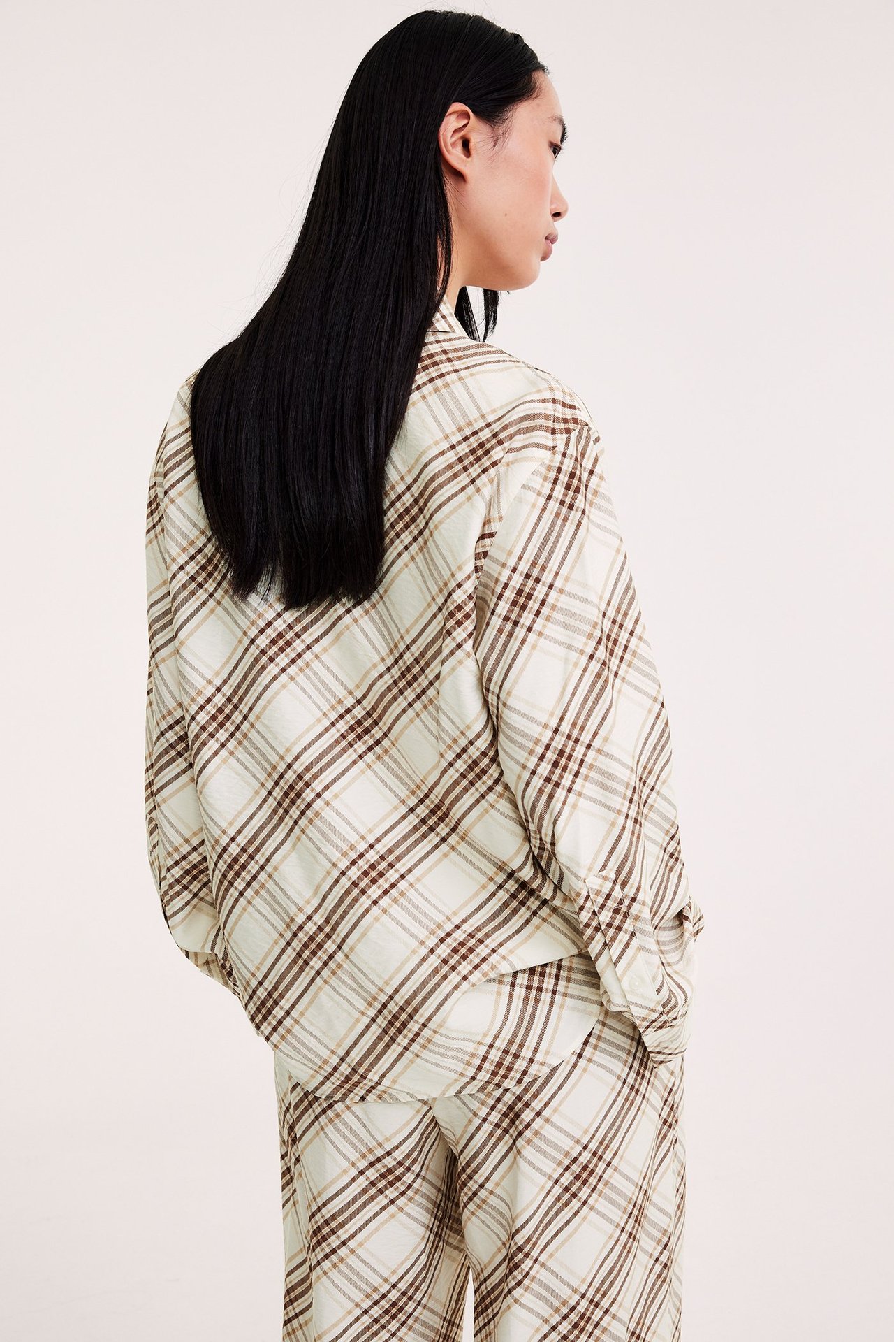 Naisen takakuva: väljä beigen ja ruskean ruudullinen viskoosisekoitepaita sekä yhteensopivat housut.