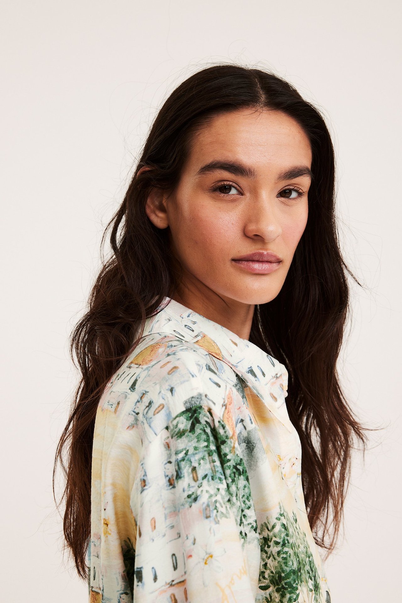 Närbild på kvinna i offwhite viskosmixskjorta med ett livfullt medelhavsinspirerat mönster.