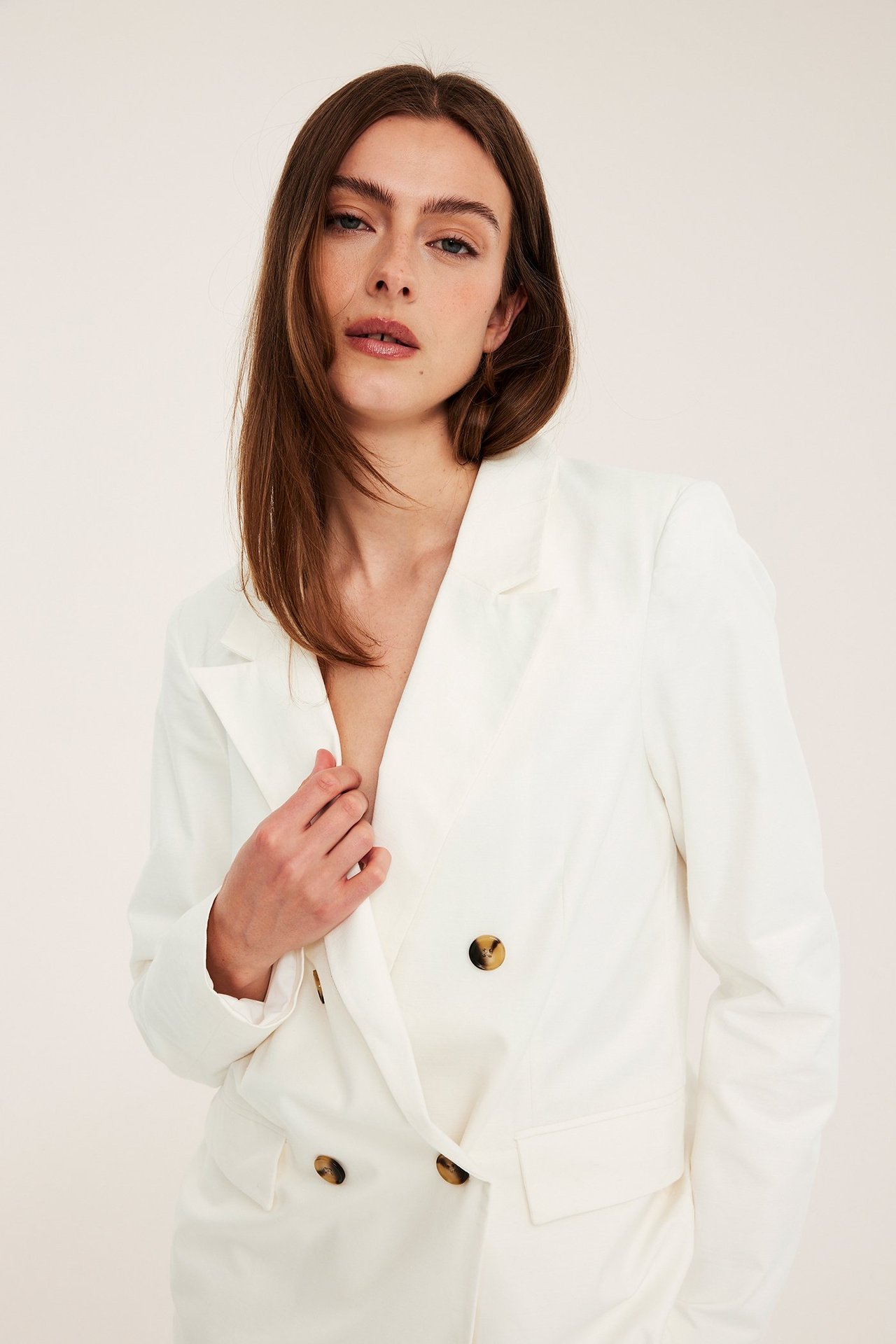 Edestä kuvattuna, nainen yllään väljä valkoinen kaksirivinen bleiseri neljällä ruskealla napilla.