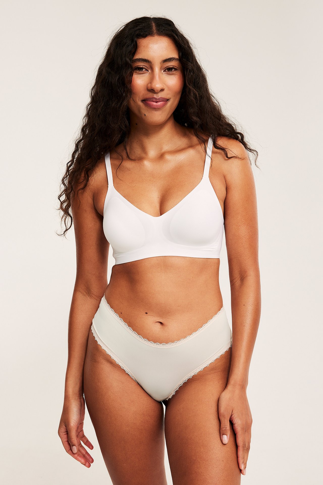 Forfra, en kvinne har på seg offwhite mikro cheeky truser med blondekant og en hvit BH.