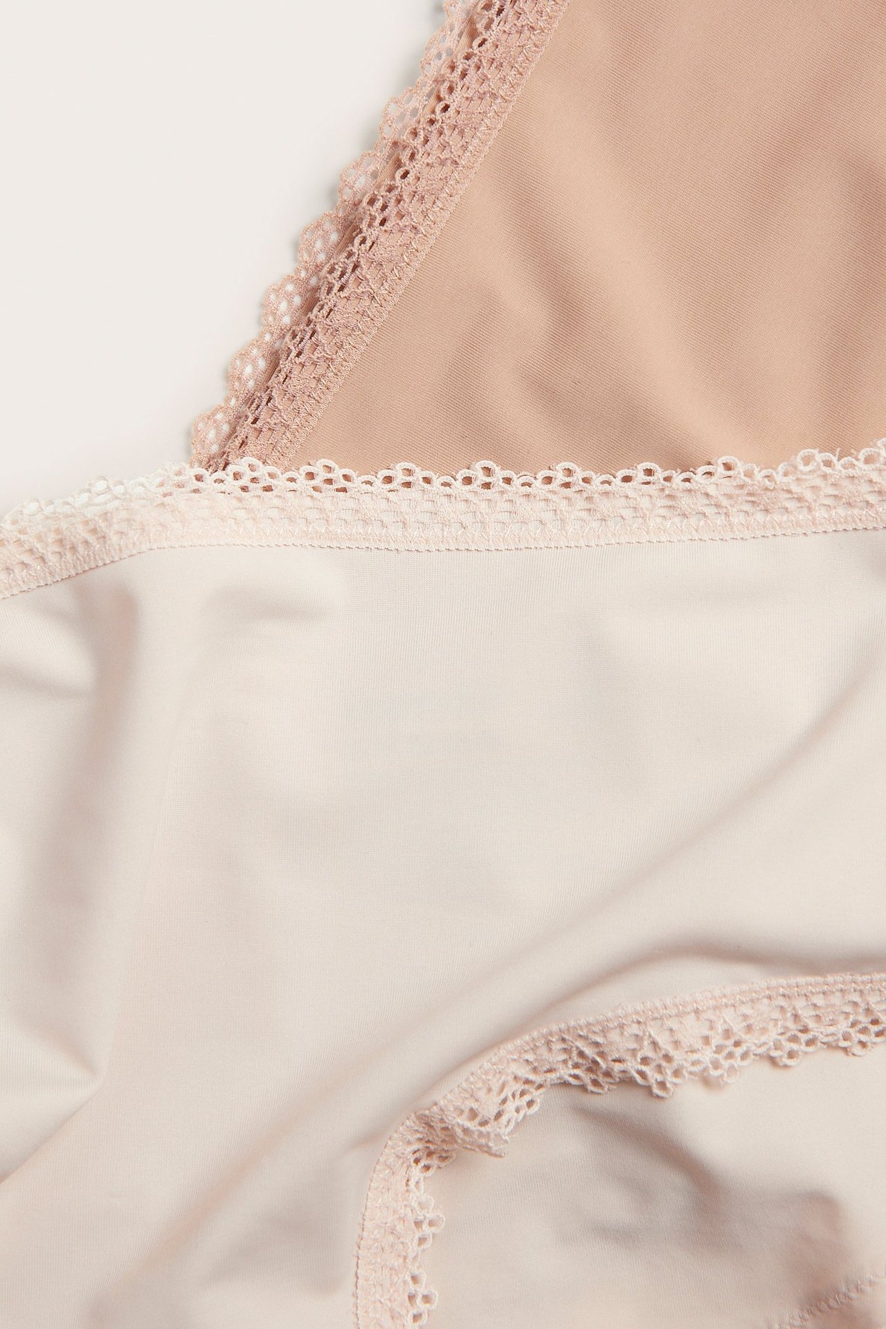 Närbild av offwhite och beiga cheeky-trosor i microkvalitet, båda med spetskant.