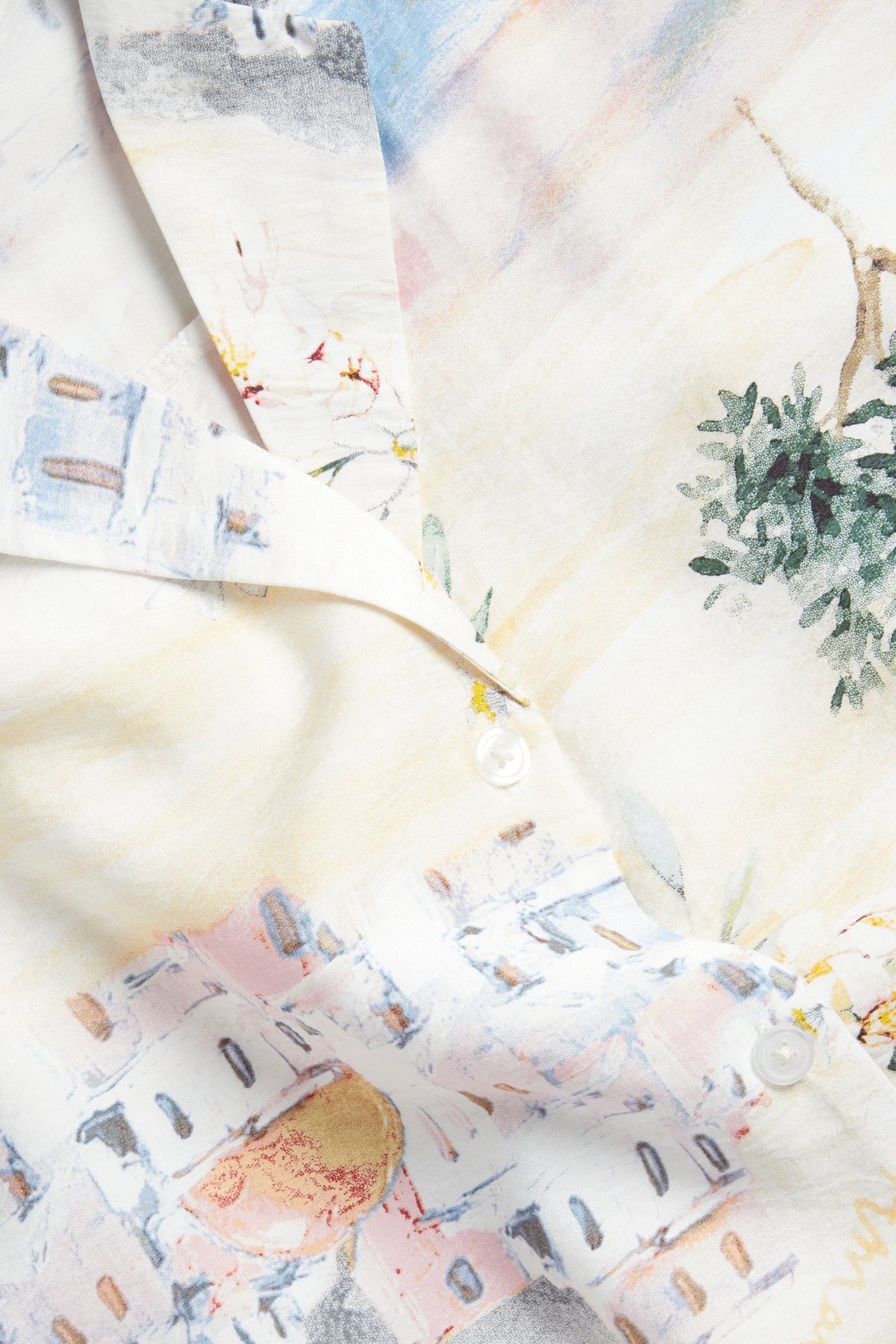 Zbliżenie na kremową wzorzystą sukienkę z krótkim rękawem, pokazujące kołnierz i białe guziki.