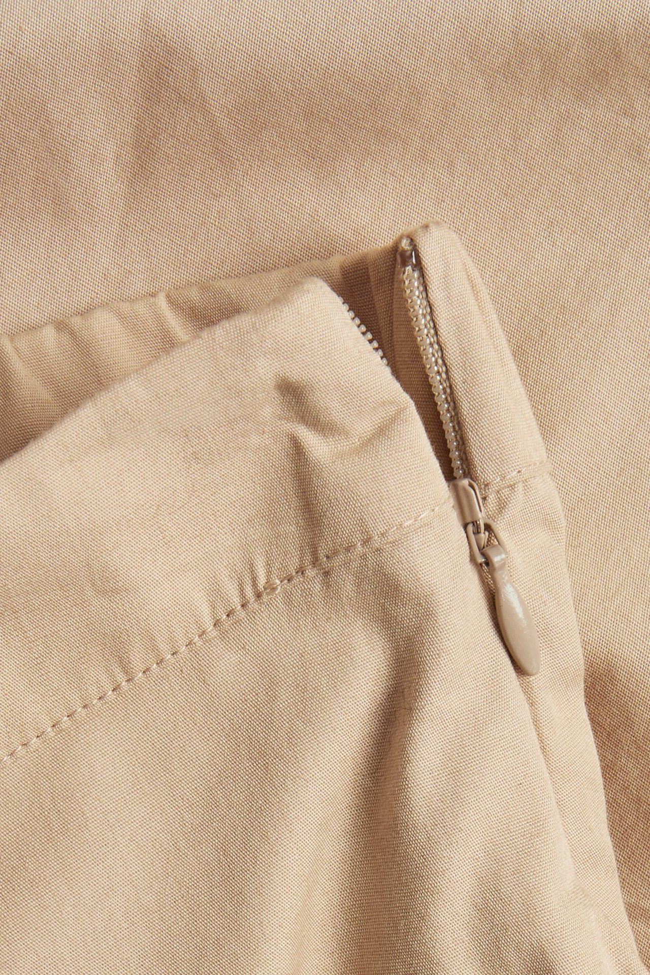 Zbliżenie beżowej spódnicy balonowej z bawełnianej popeliny z widocznym bocznym zamkiem i marszczeniami.