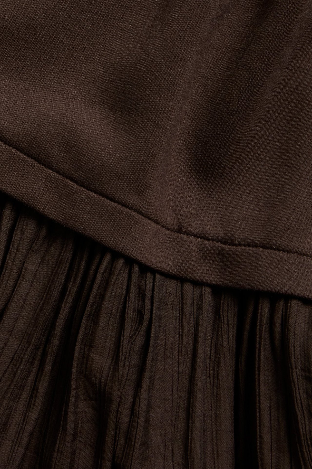 Närbild av en mörkbrun långklänning med jerseytop och vävd, krinklad kjol.