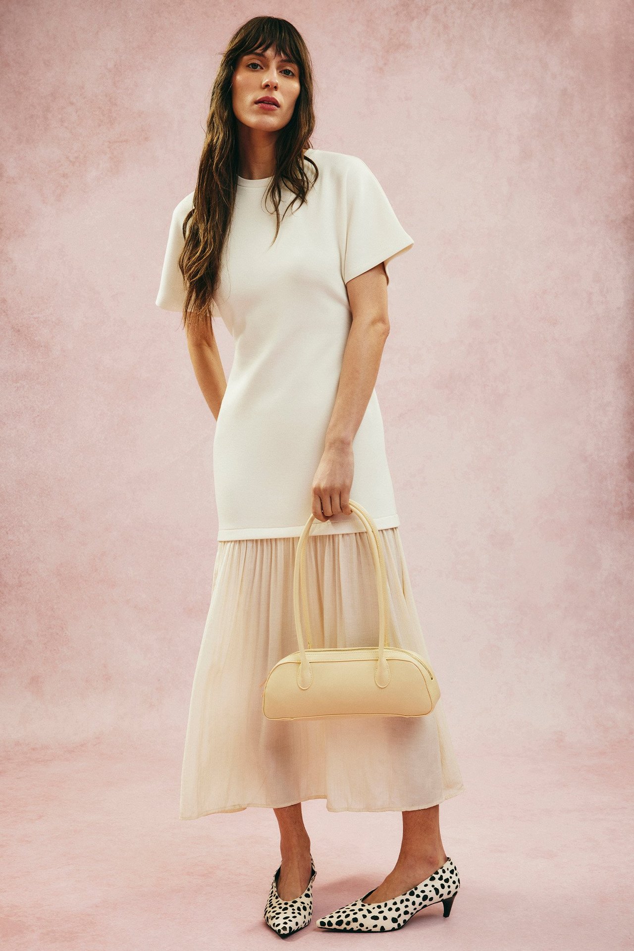 Widok z przodu: kobieta w kremowej długiej sukience z krótkim rękawem, trzyma jasną żółtą torebkę, buty w cętki.