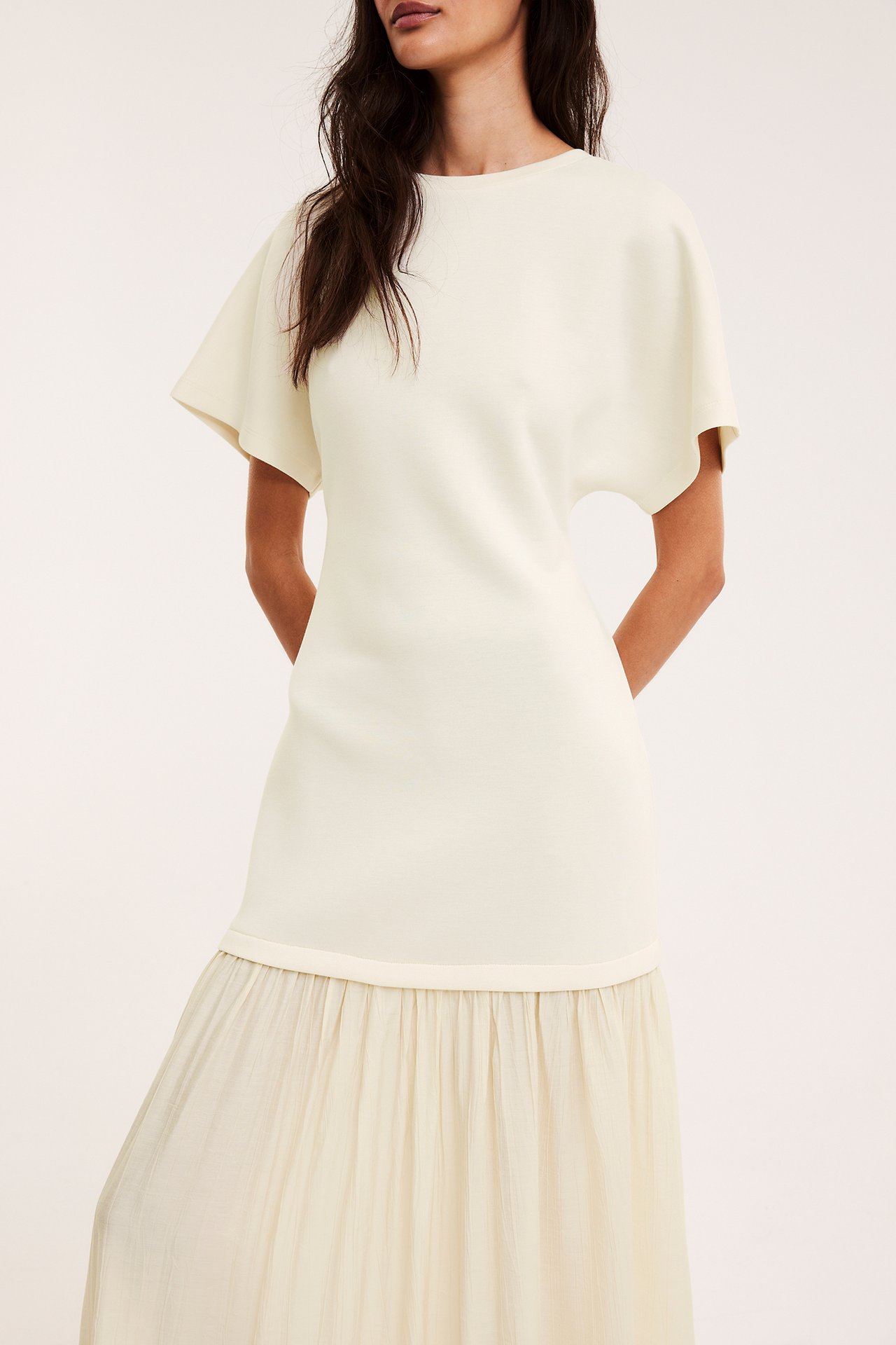 Frontvy av kvinna i en offwhite långklänning med jerseytop och vävd, rynkad kjol.