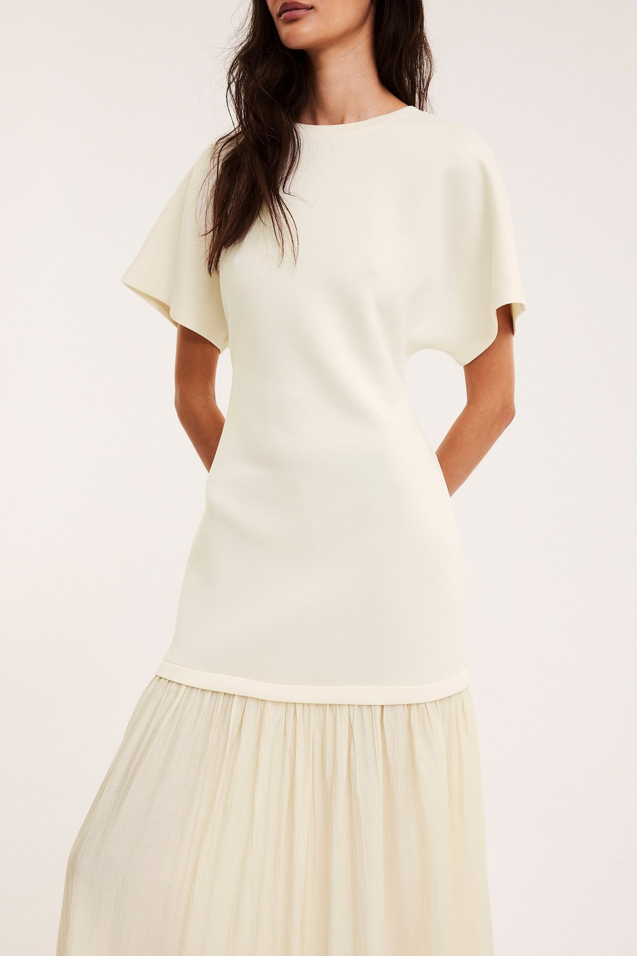 Widok z przodu kobiety w kremowej długiej sukience z dżersejową górą i tkaną, marszczoną spódnicą.