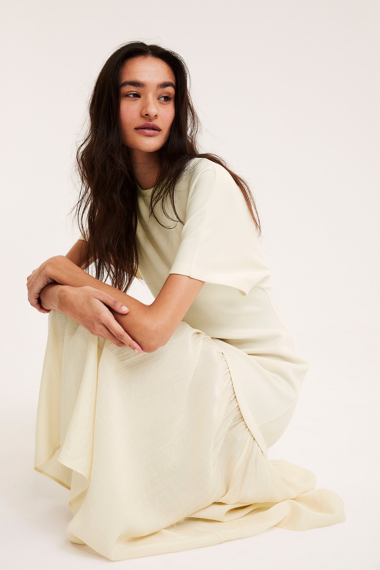 Widok z przodu kobiety w kremowej długiej sukience z krótkim rękawem z dzianinowym topem i tkaną spódnicą.