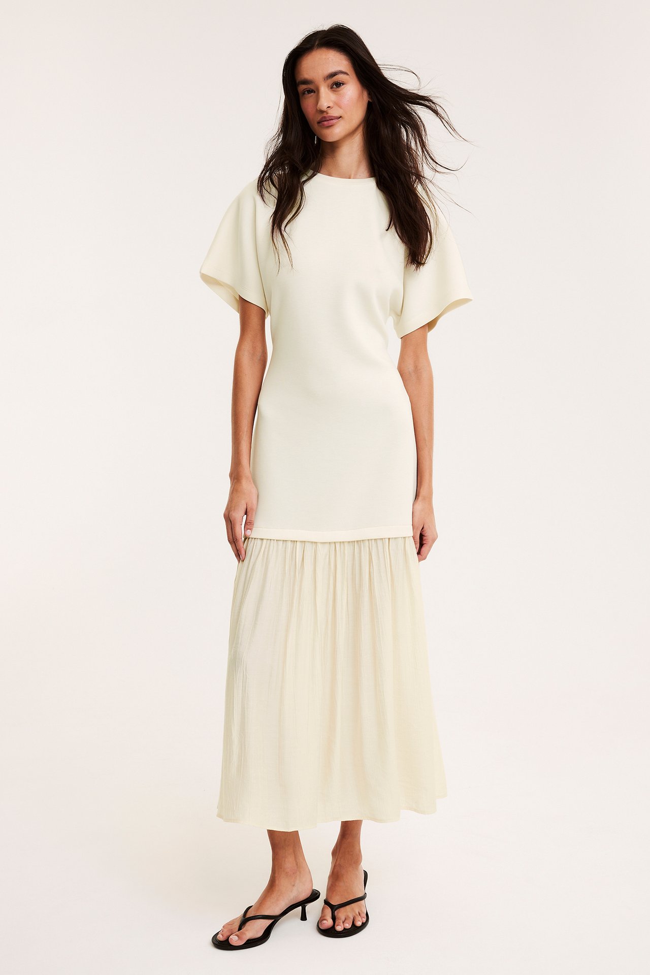 Framsida: Kvinna i offwhite långklänning med jerseytop, vävd kjol och svarta string-sandaler.